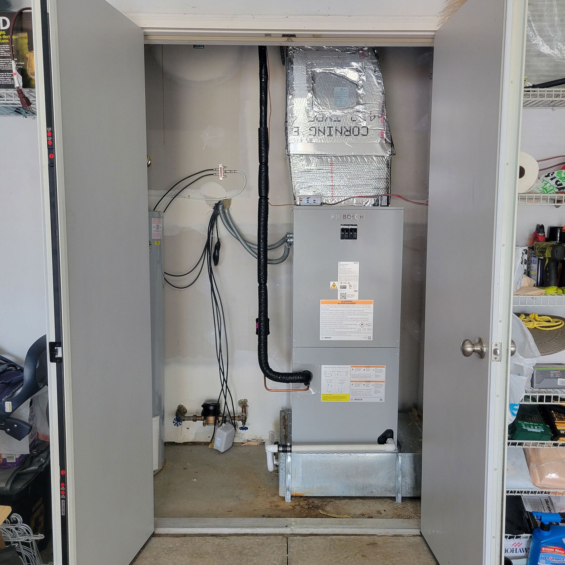 Open furnace closet with gray HVAC unit, ducts, and exposed pipes behind partially open doors
