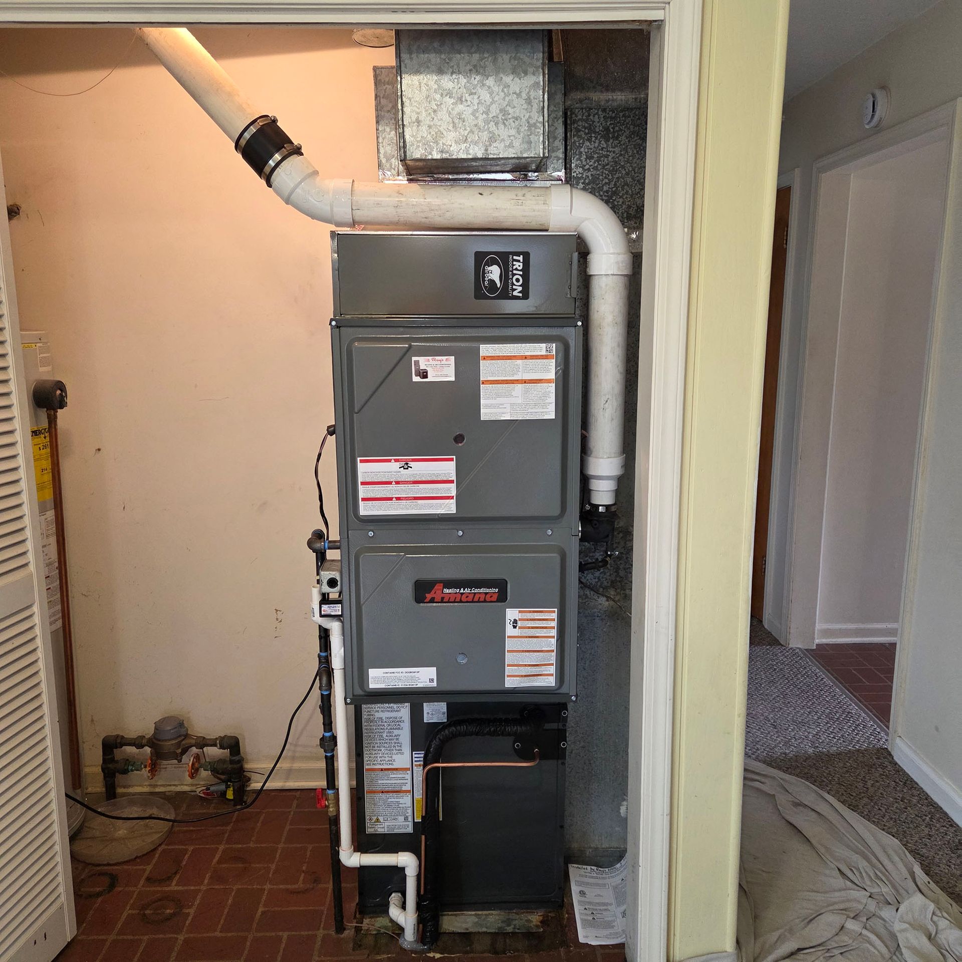Grey furnace and HVAC unit in a hallway closet with exposed ductwork and tiled floor.