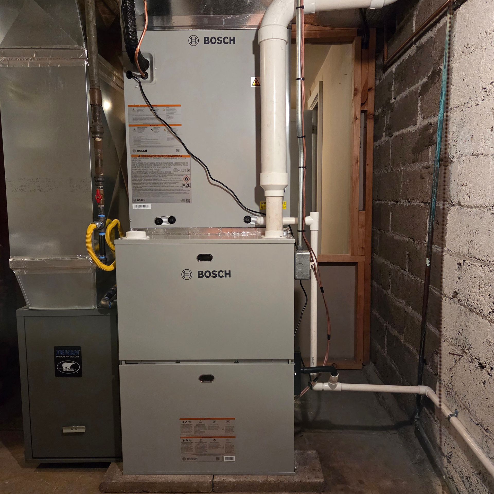 Bosch furnace and water heater in a basement utility area with exposed pipes and brick walls