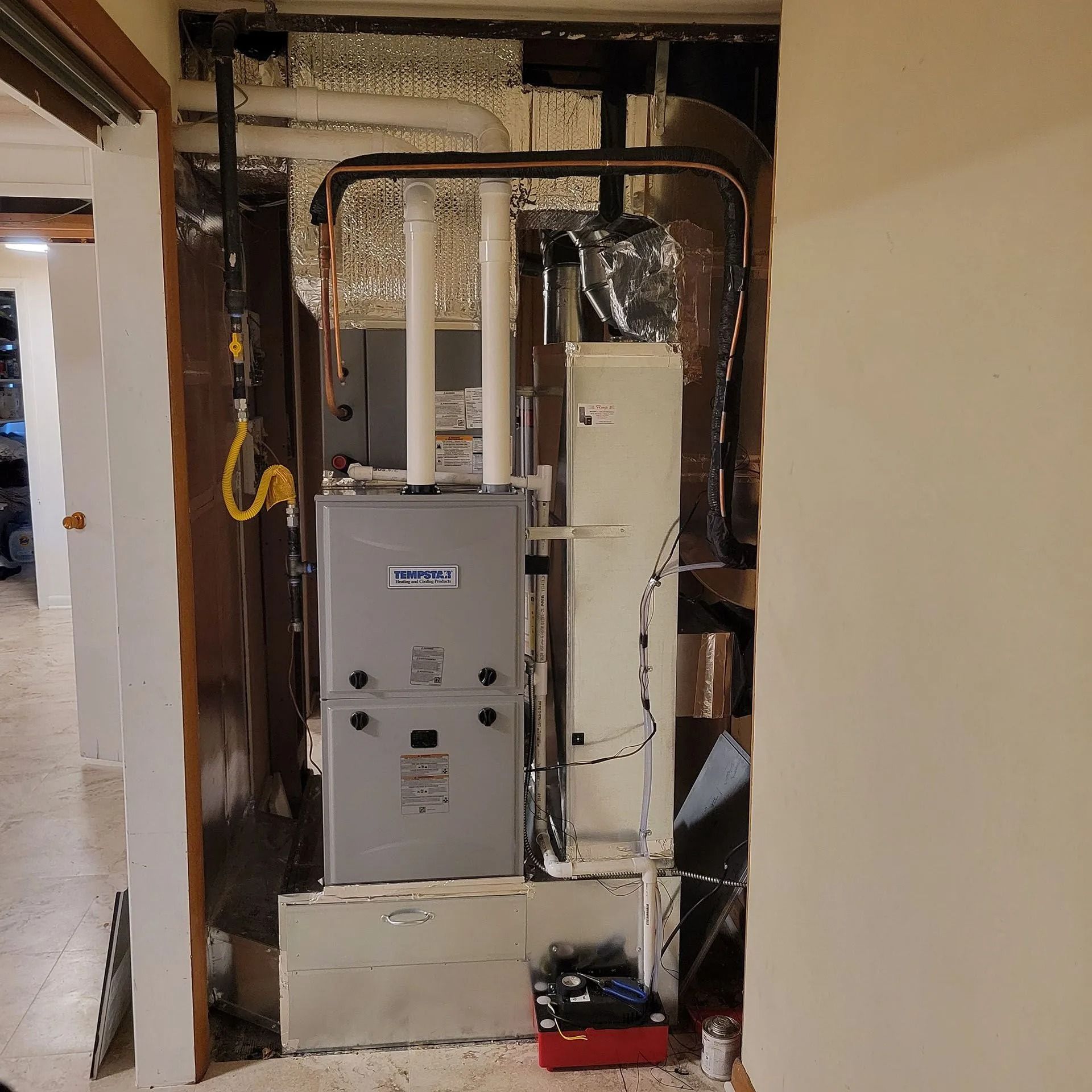 New furnace installed in an unfinished wall cavity with exposed ductwork and wiring.