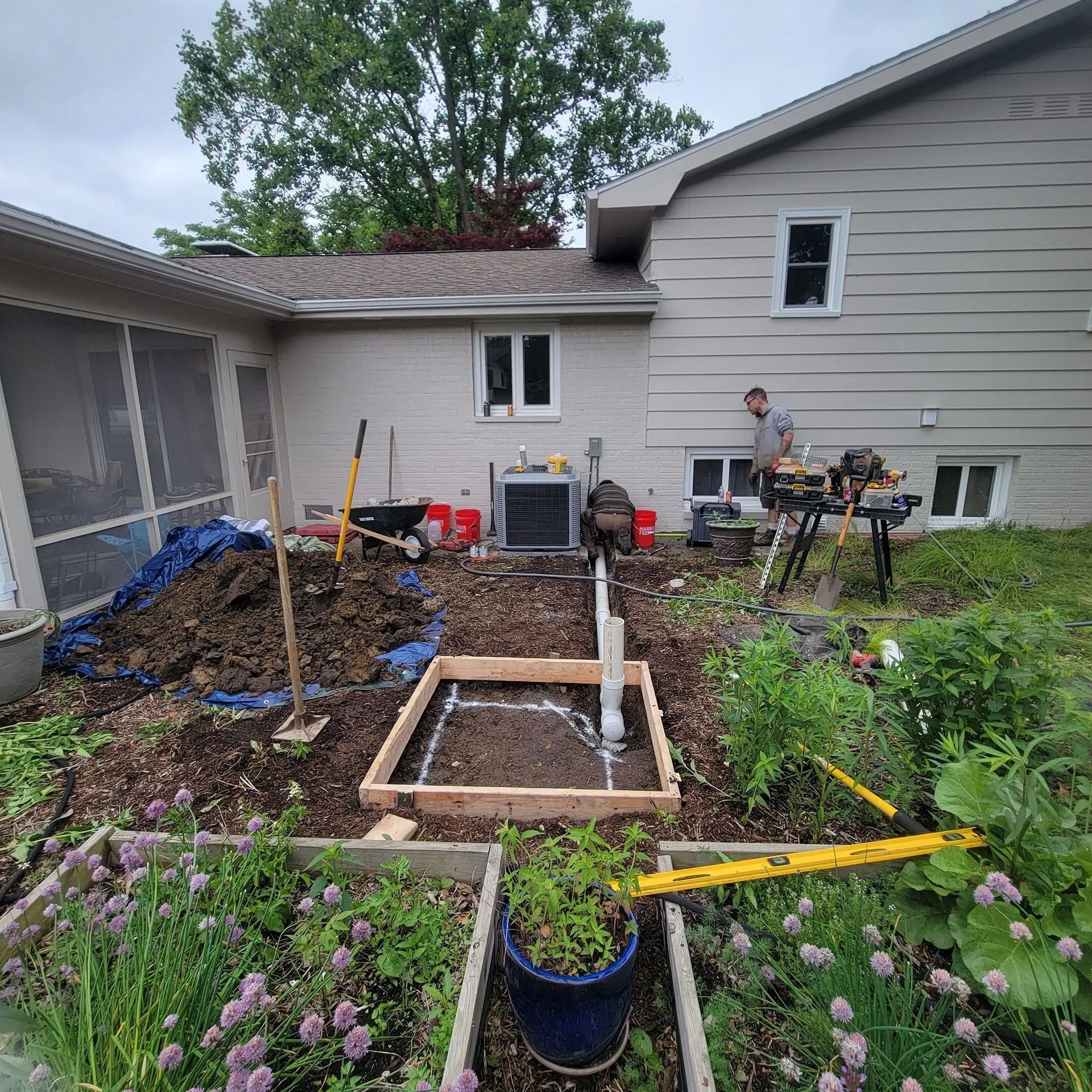 Backyard garden renovation with raised bed framing, soil piles, and a person working near a house
