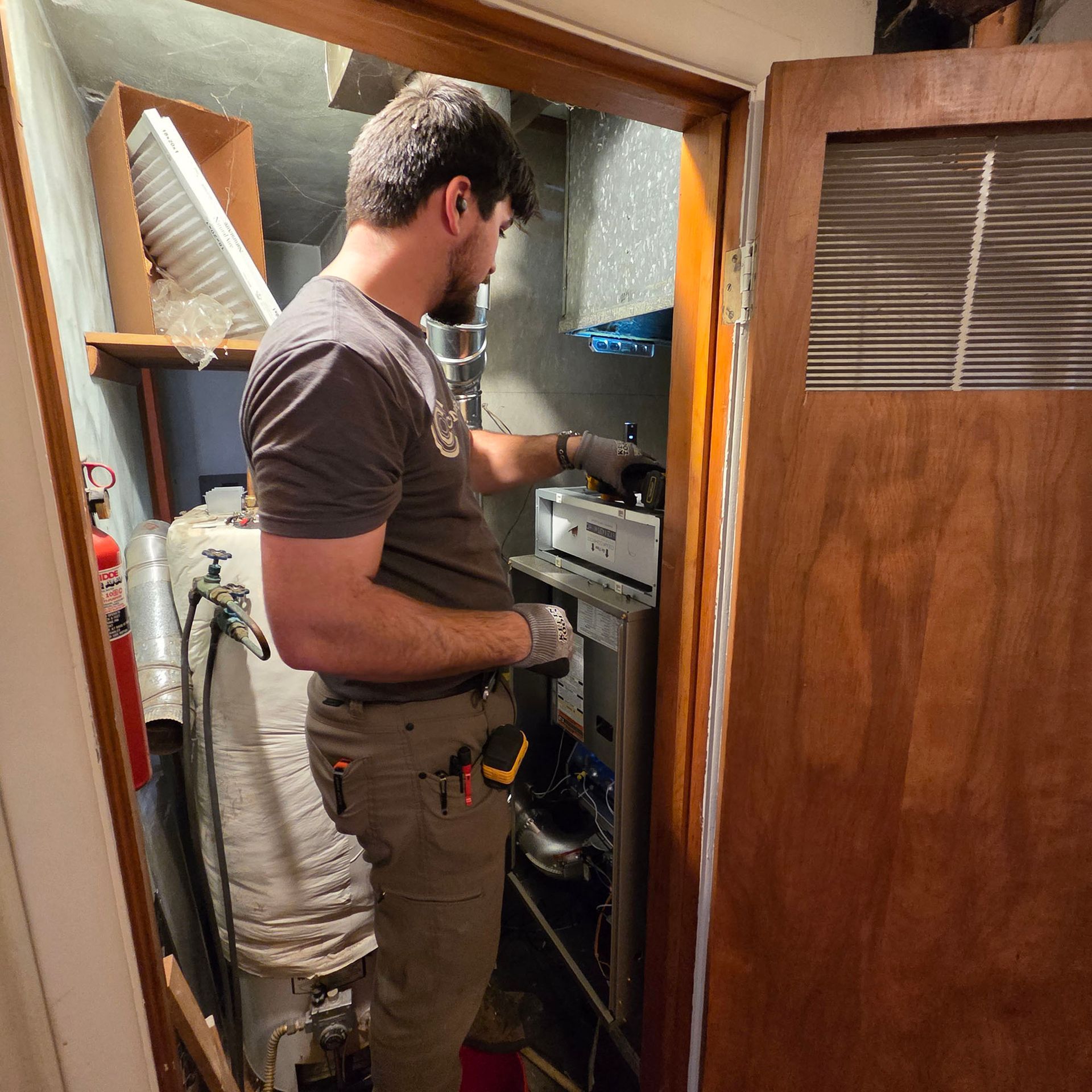 Technician working on a furnace in a narrow closet utility space