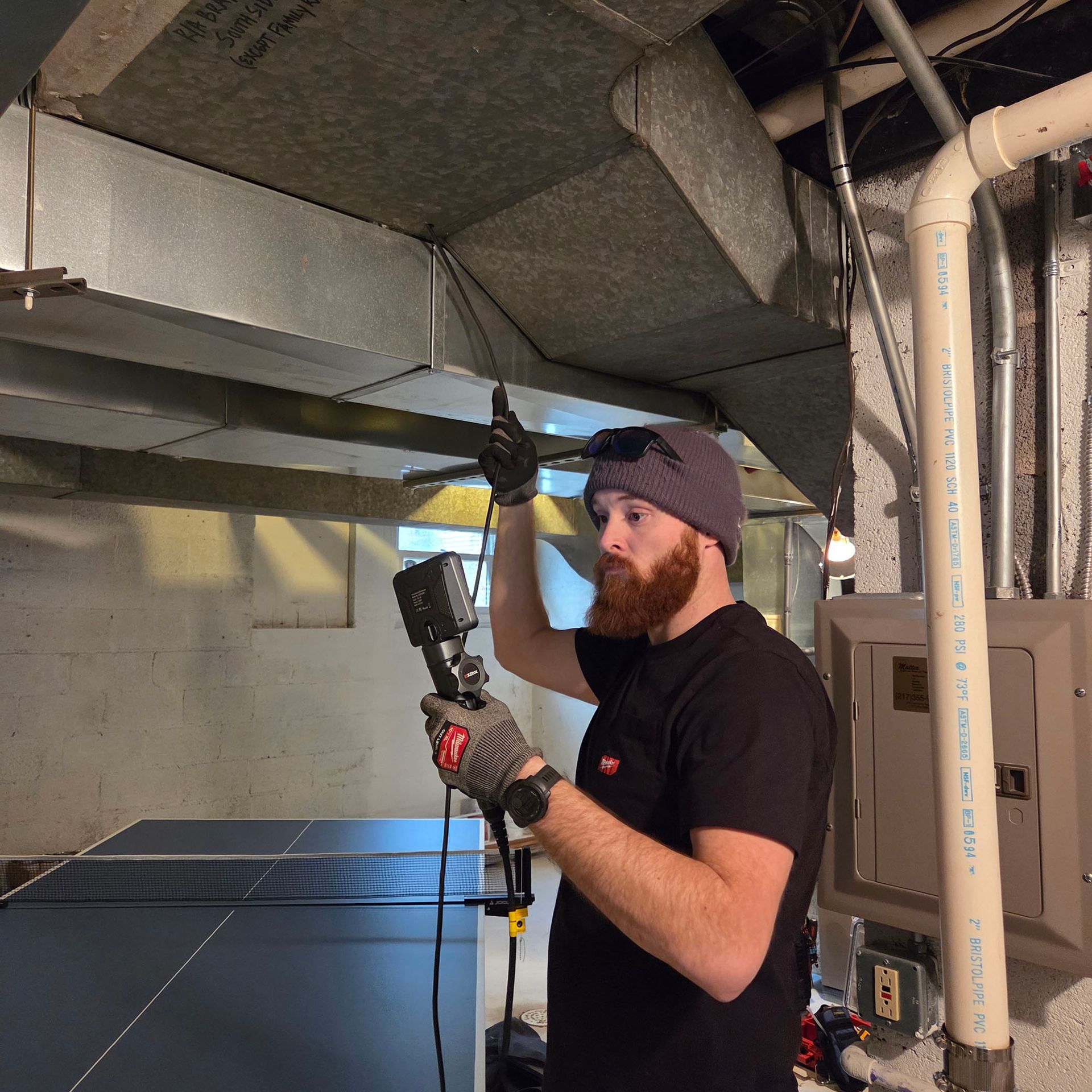 Technician inspecting ceiling ductwork with a flashlight in a basement utility room