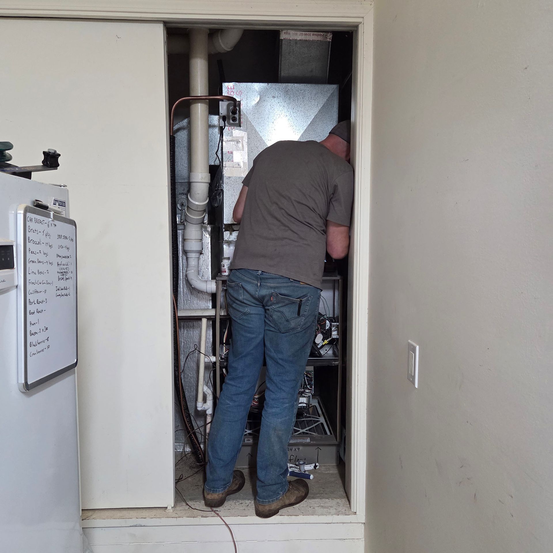 Worker inspecting equipment in a utility closet doorway, with pipes and wiring visible inside.