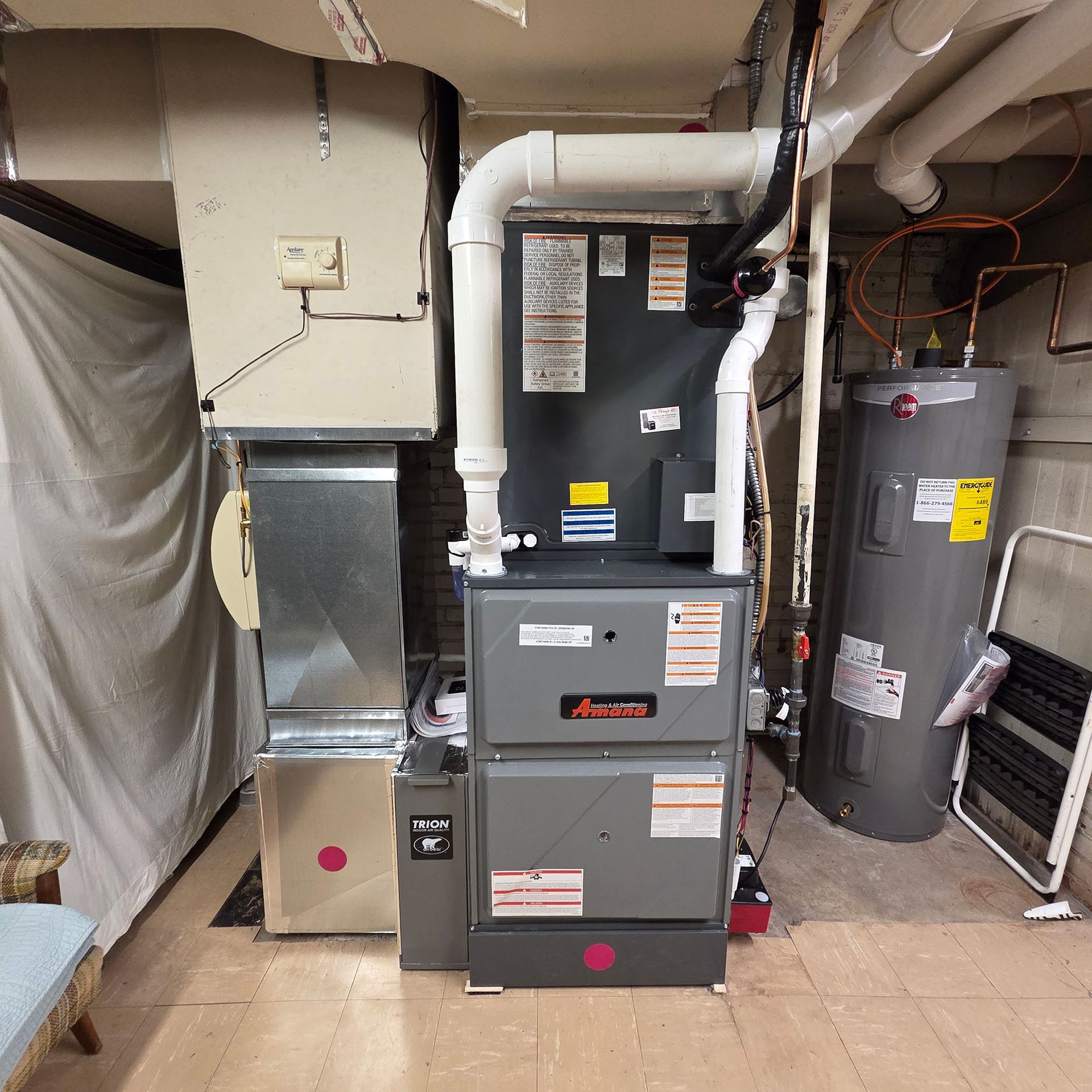Basement furnace and HVAC system with ductwork, pipes, and a water heater lined along the wall.