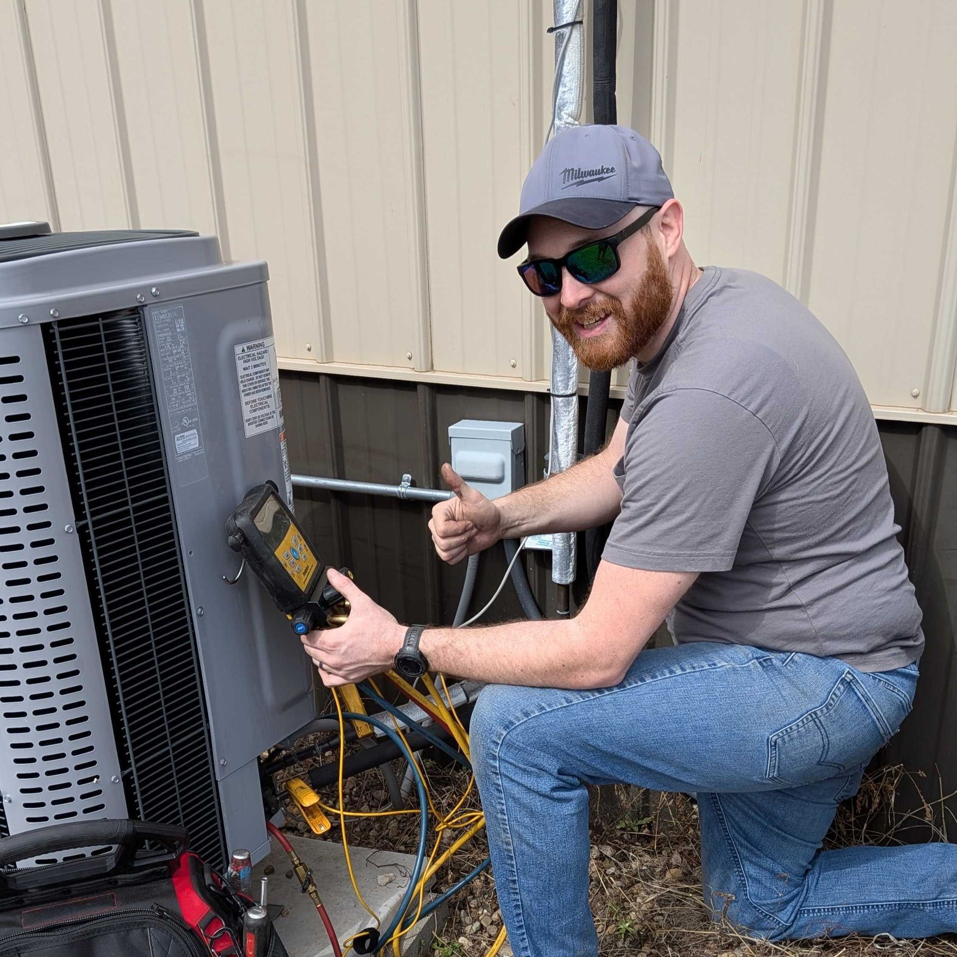 Technician testing an outdoor HVAC unit with a multimeter beside a beige building.