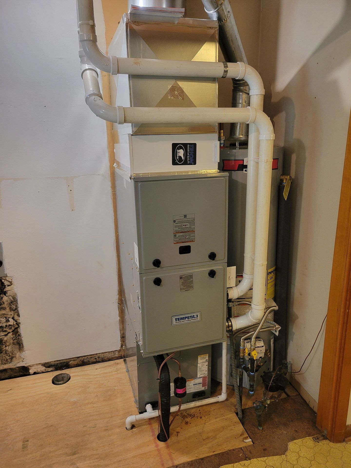 Basement furnace with white ductwork and pipes beside a wall and concrete floor.