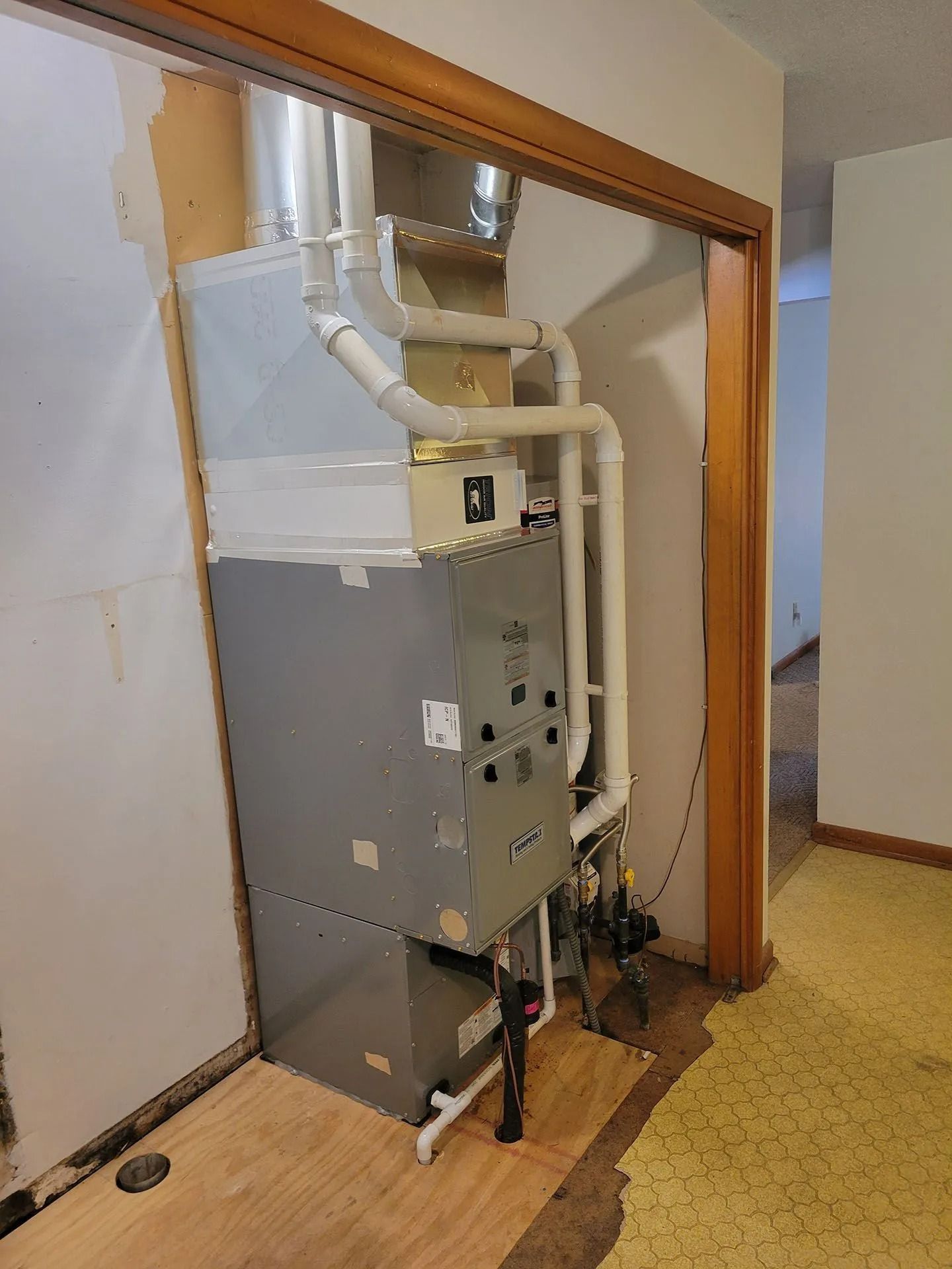 HVAC furnace and ductwork in a hallway closet with exposed pipes and a metal access panel