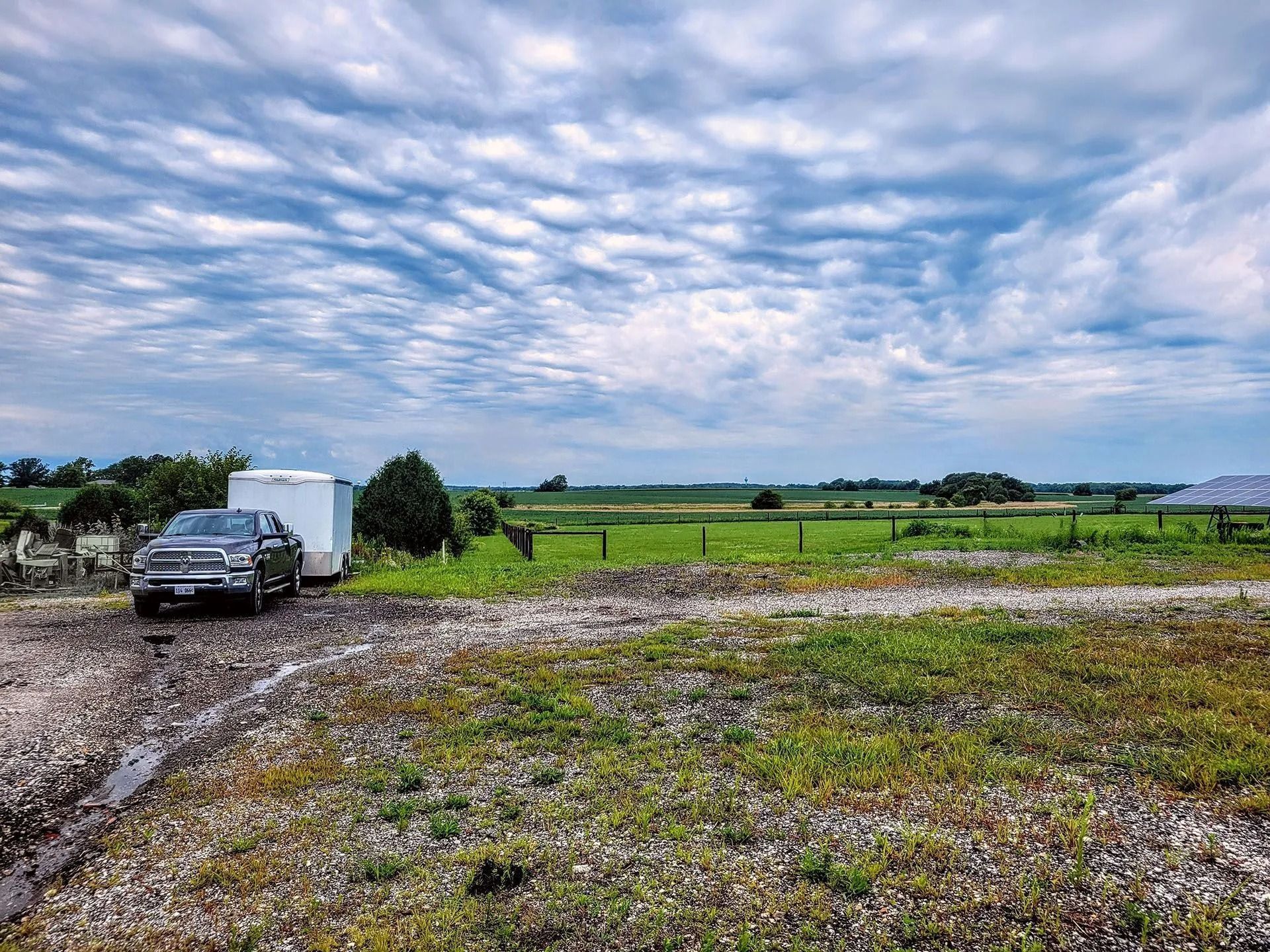 Parked truck beside a gravel road in a wide green field under a cloudy sky