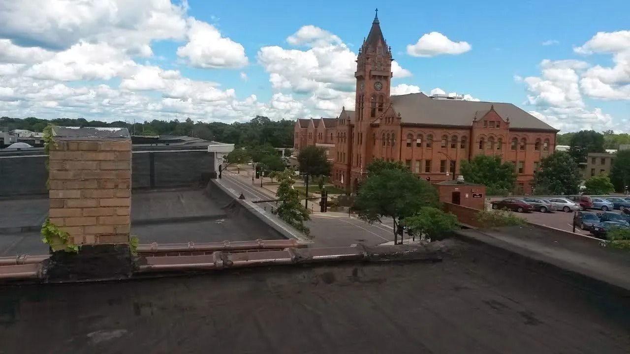 Rooftop view of a red-brick historic building with a tall tower under a cloudy sky.