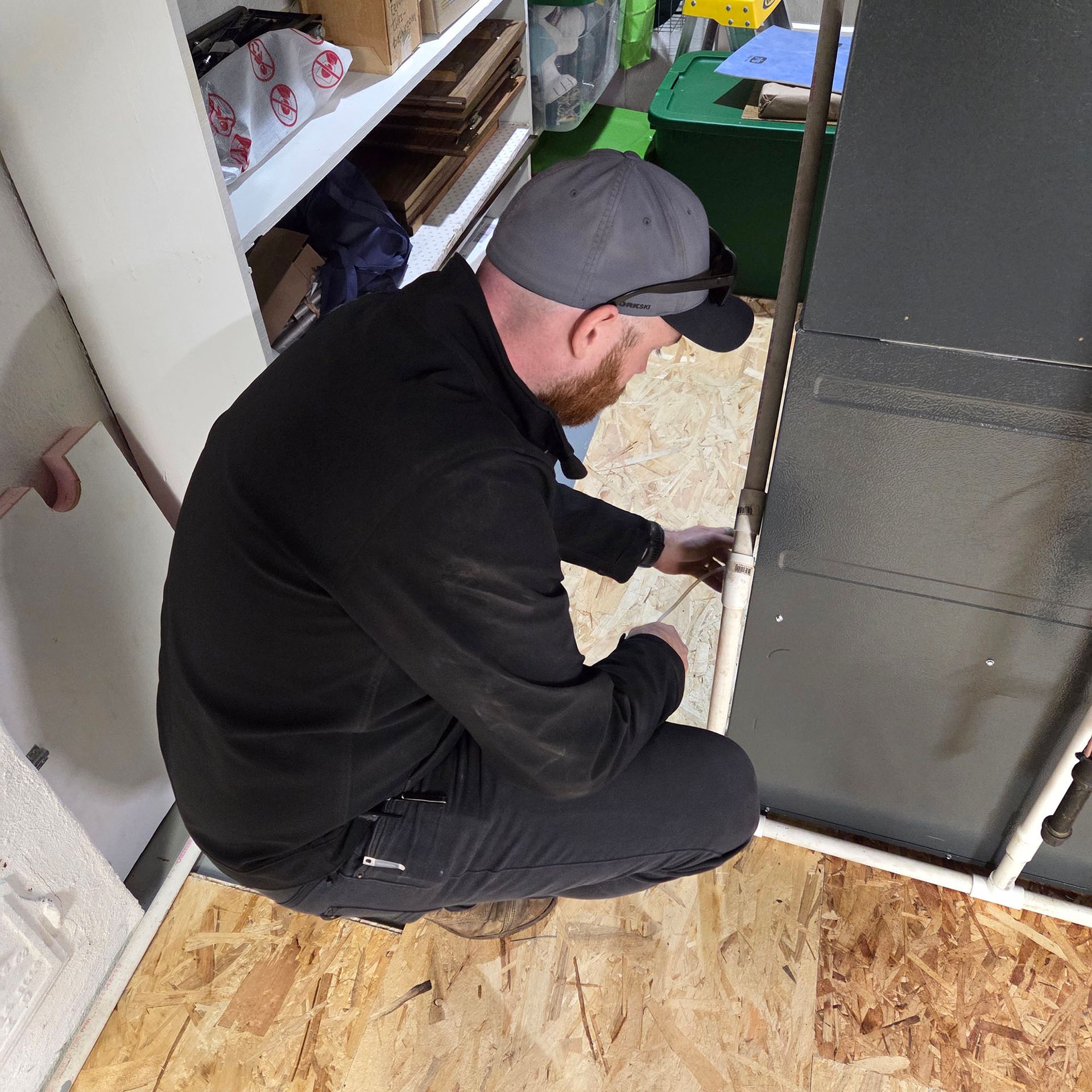 Worker crouches beside a wall, using a tool to install trim in an indoor workspace.