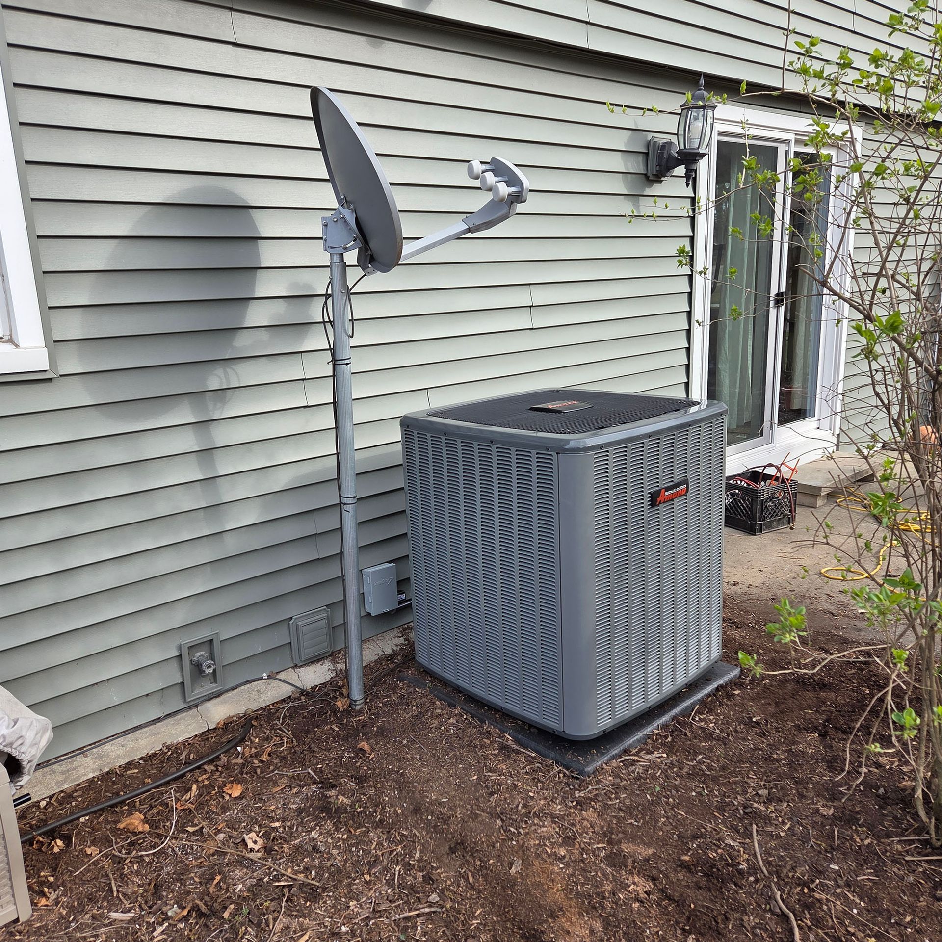 Outdoor HVAC unit beside a house with a satellite dish mounted on the wall.