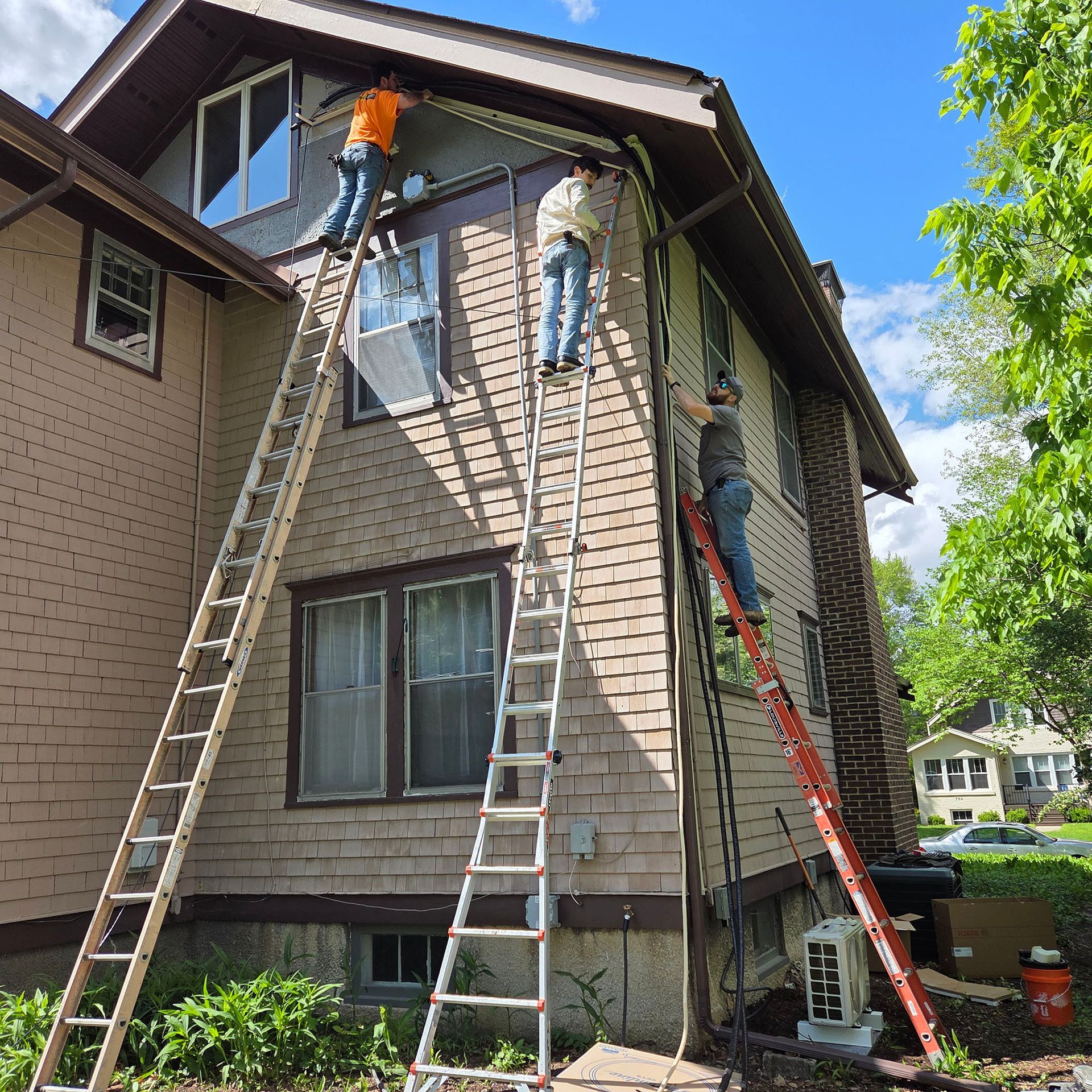 Workers on ladders repairing the roof and siding of a two-story house