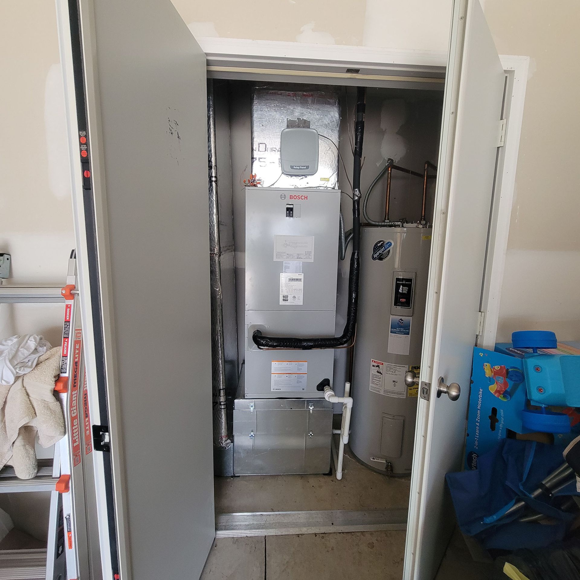 Open utility closet with a furnace and water heater inside, partially blocked by open doors.