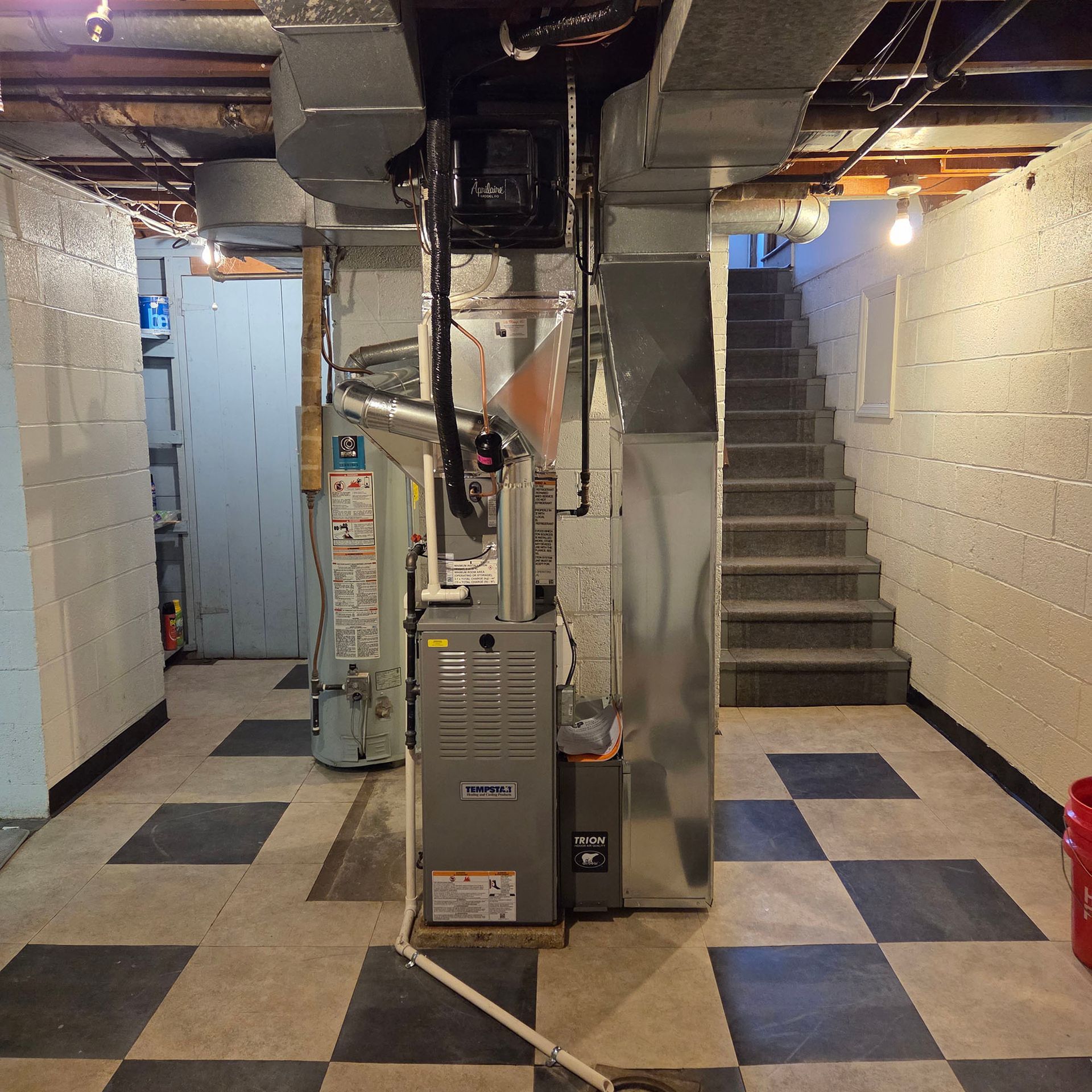 Basement utility room with furnace, exposed pipes, stairs, and checkered tile floor