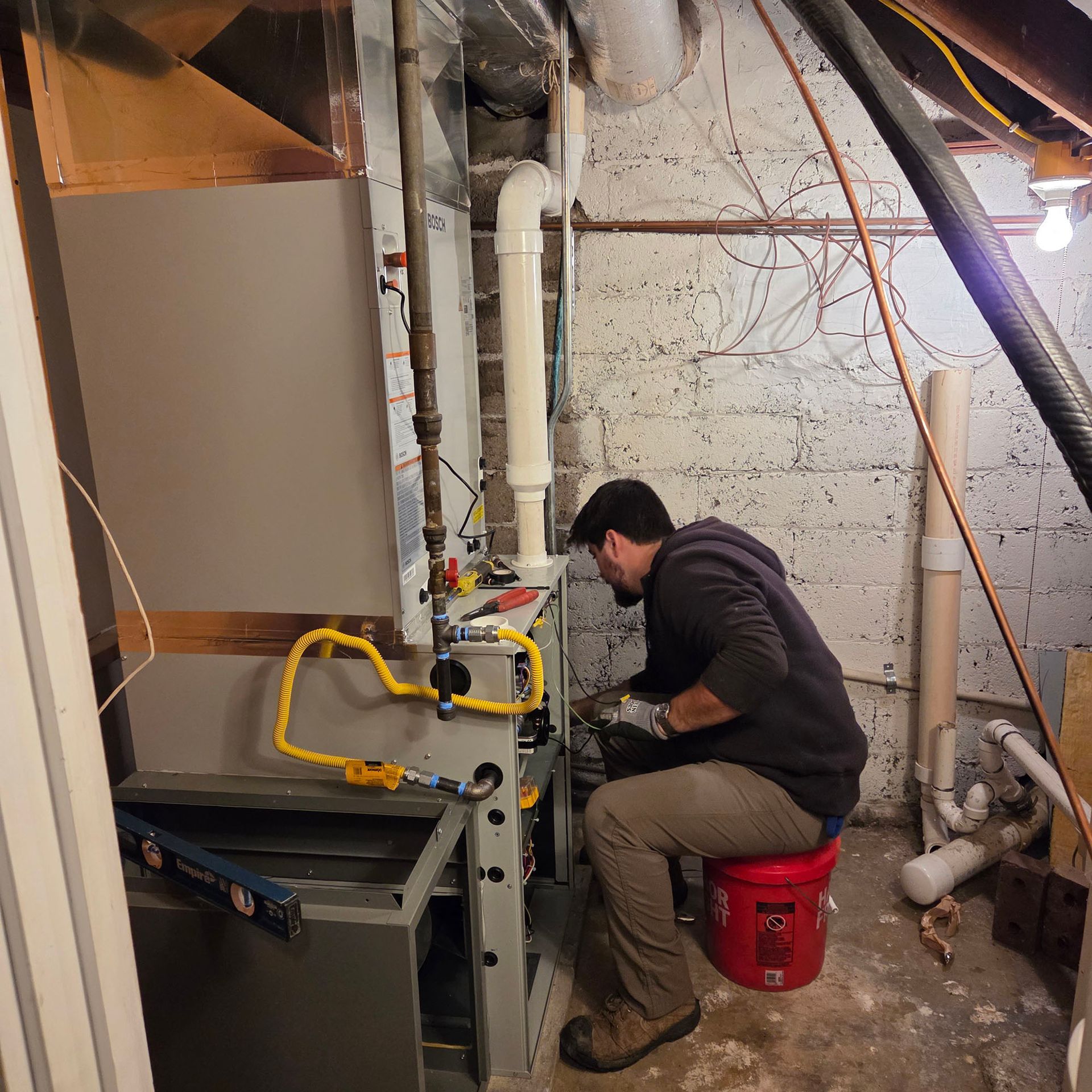 Person working on HVAC equipment in a cramped basement utility room.
