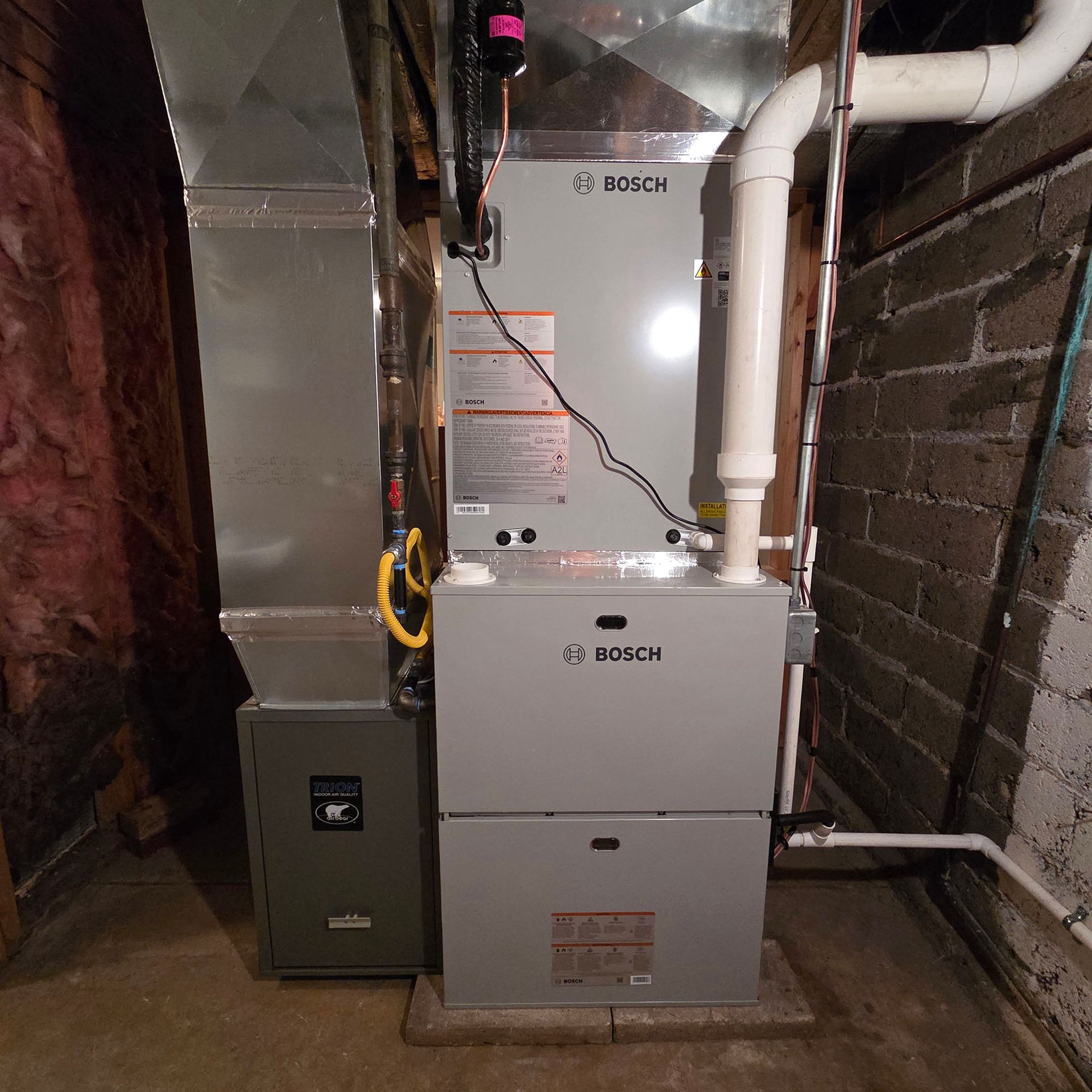 Bosch furnace and water heater in a narrow basement utility area with exposed ductwork and pipes