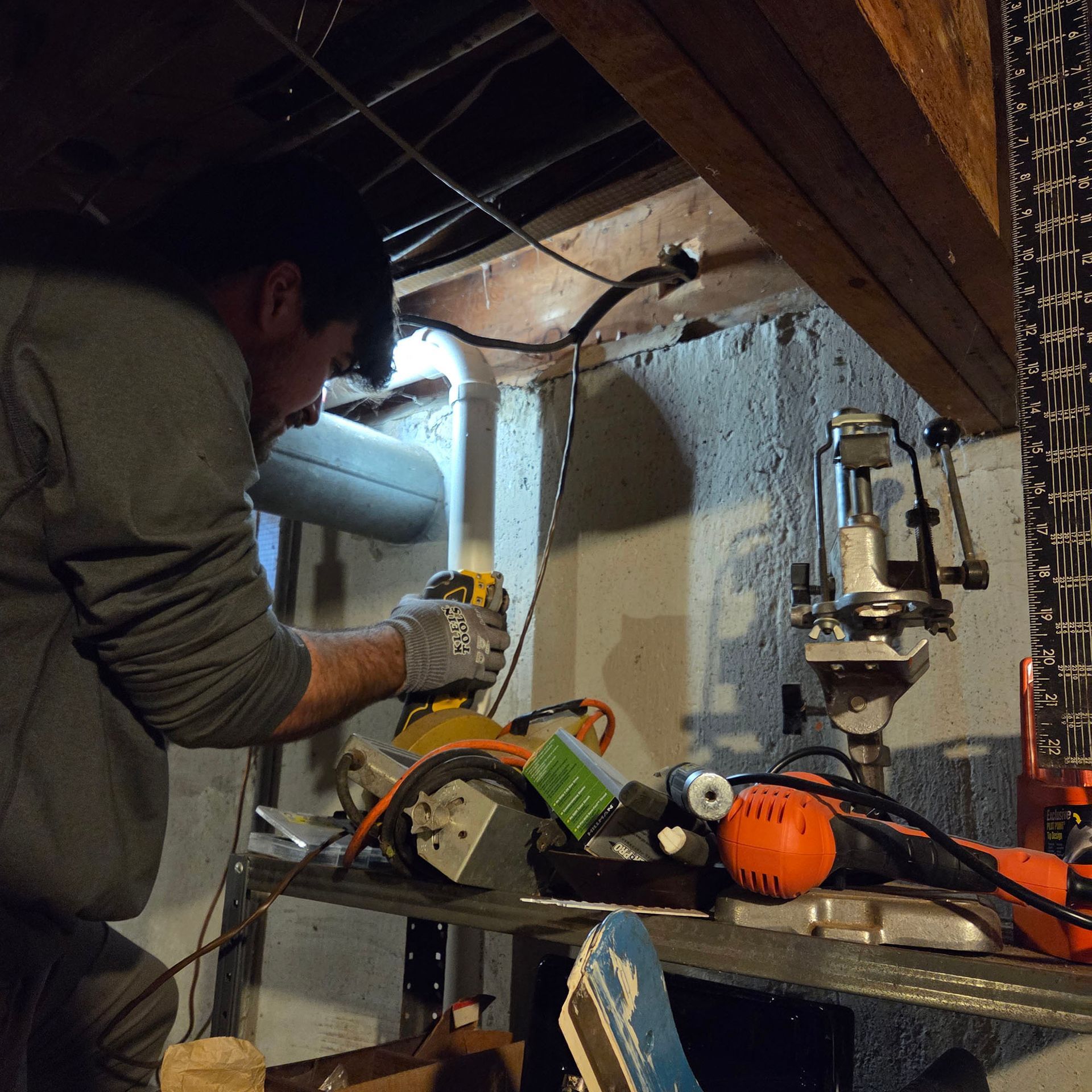 Person using a power saw in a cluttered basement workshop, with tools and pipes nearby.