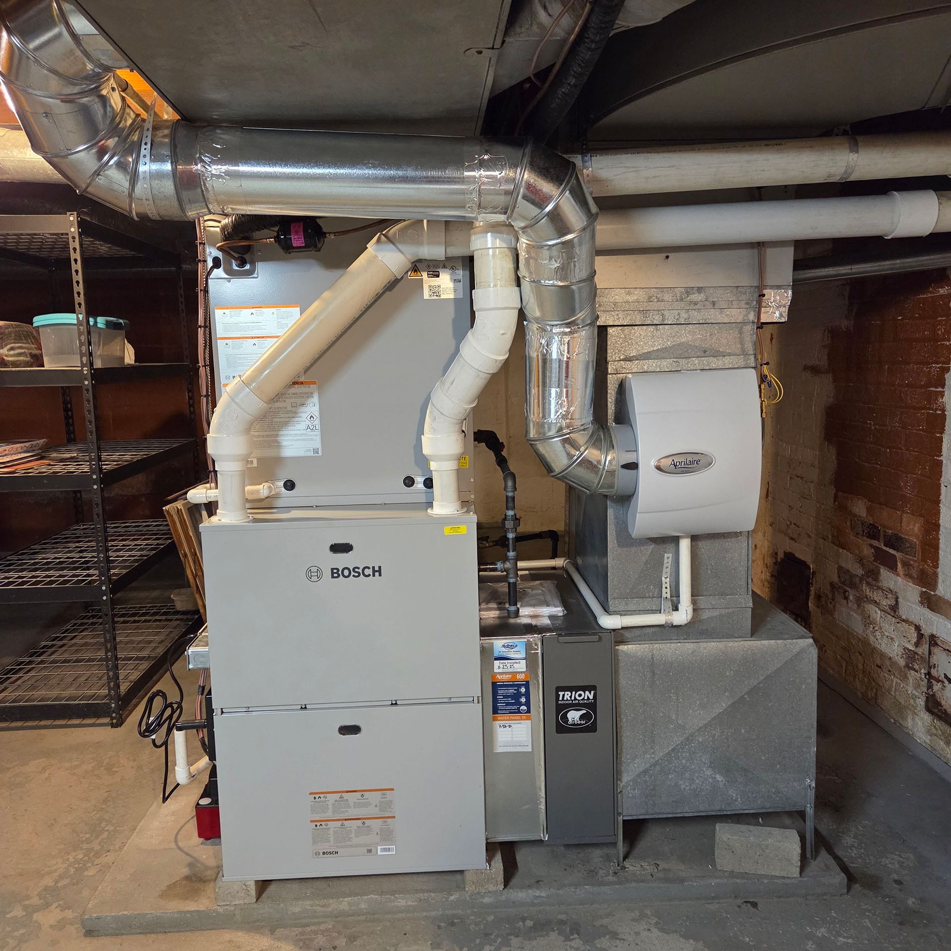 Basement furnace and HVAC ductwork with metal vents, white and gray equipment, and brick walls