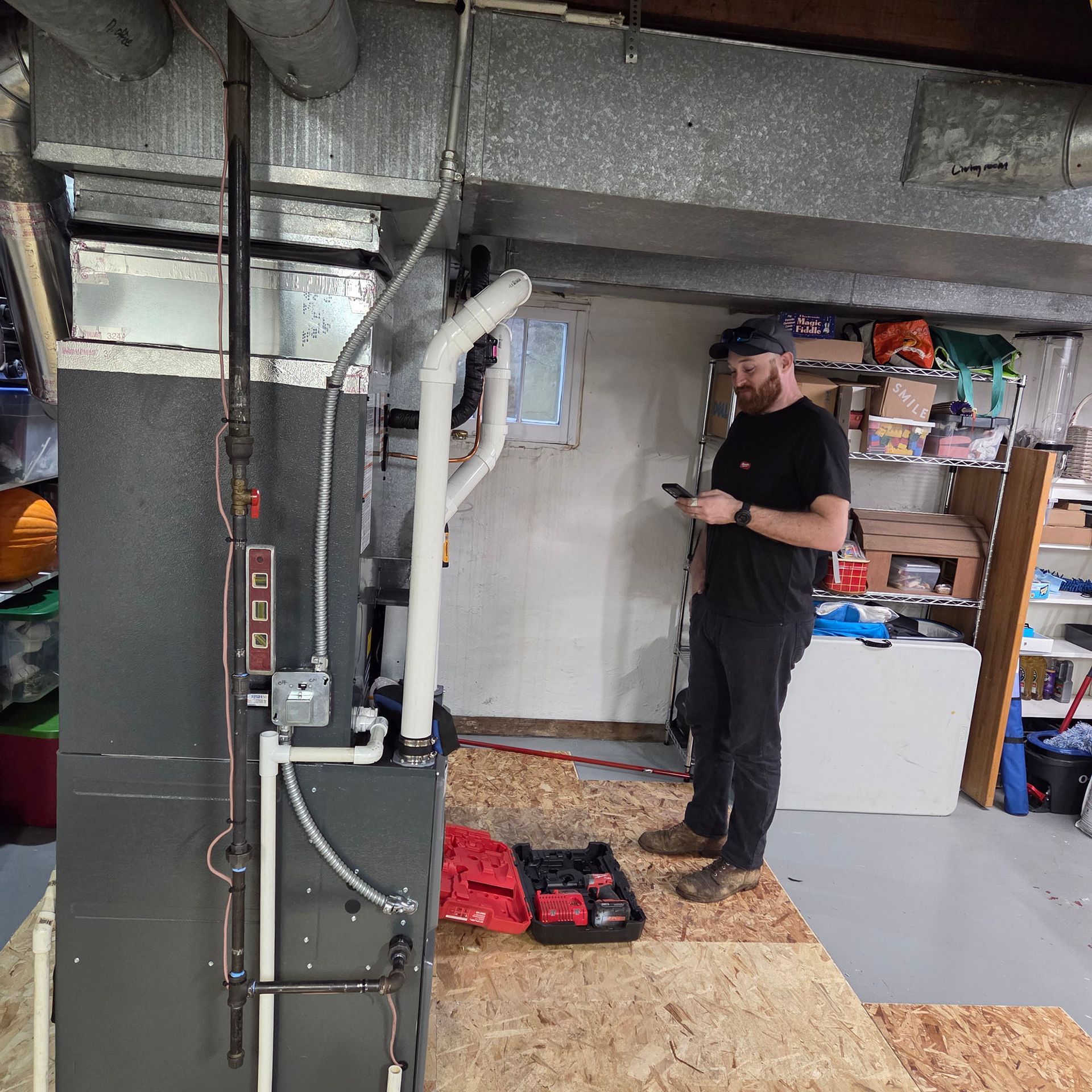 Technician standing in a basement utility room beside HVAC equipment and exposed pipes.