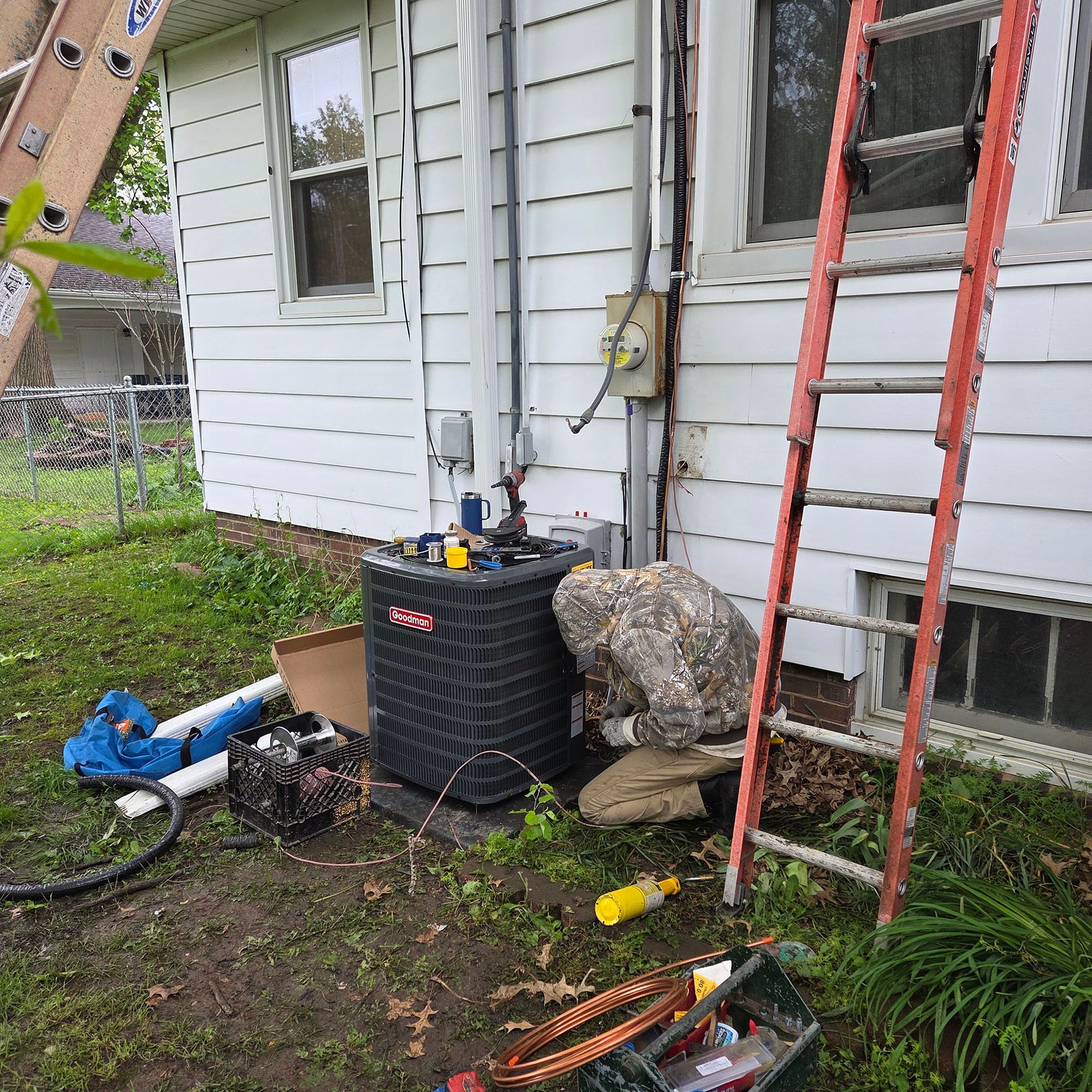 House exterior with HVAC unit, ladder, and tools scattered on muddy ground by the wall
