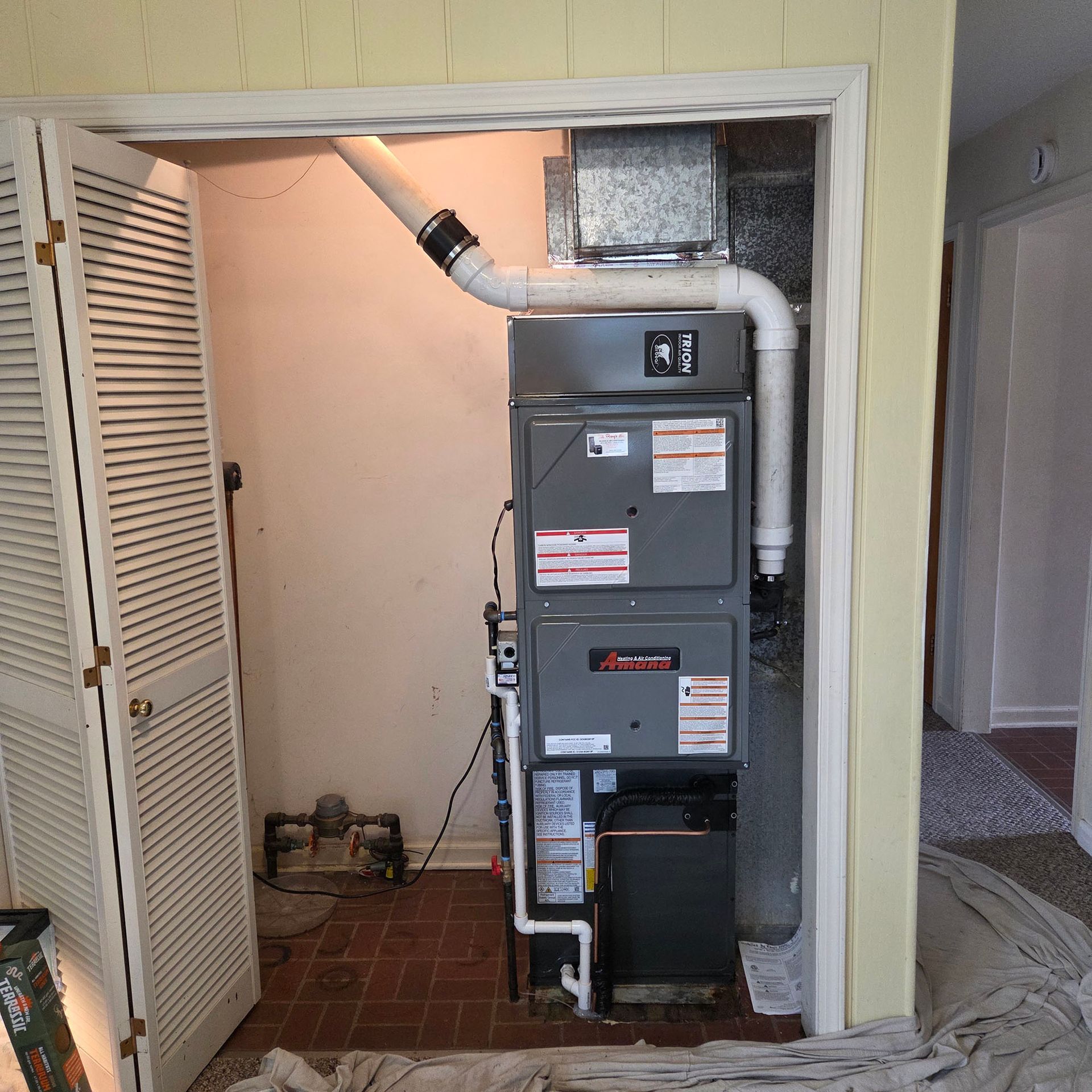 Residential furnace and ductwork in a closet, with white vent pipe and tiled floor.