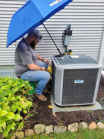 Technician under blue umbrella servicing outdoor air conditioner beside house siding