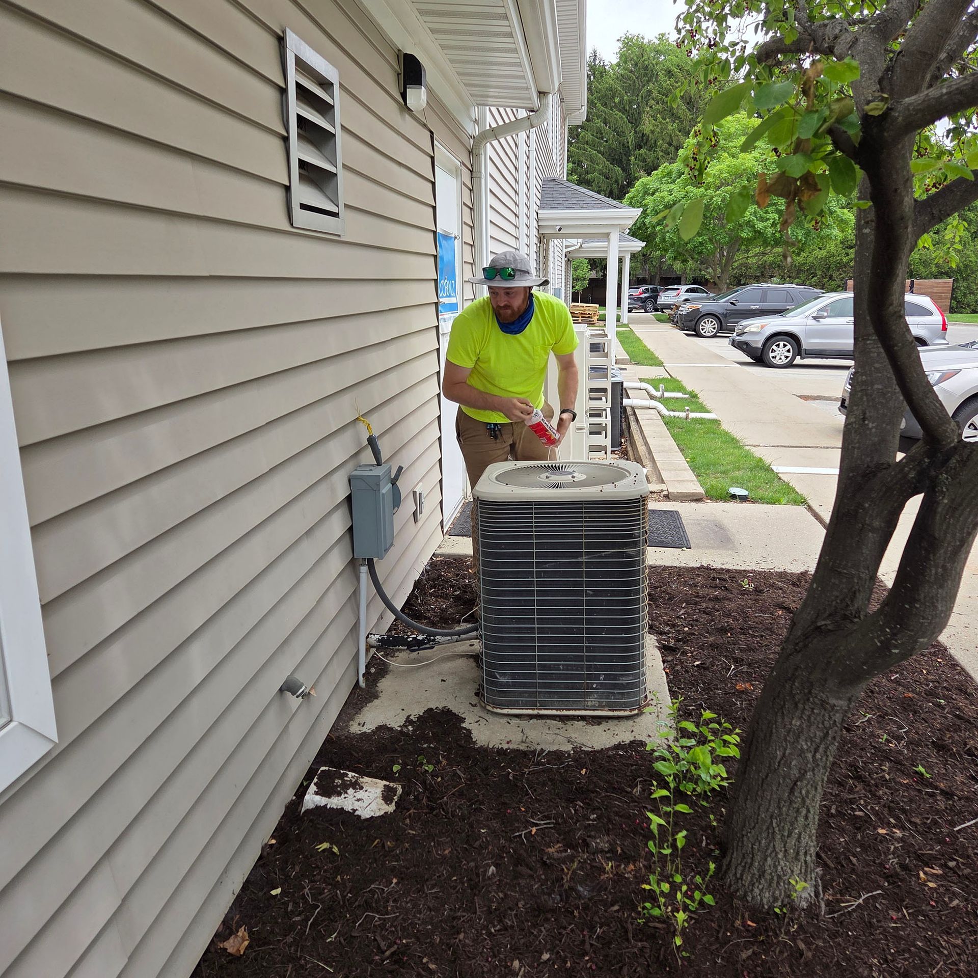 Worker in neon shirt servicing an outdoor HVAC unit beside a house.