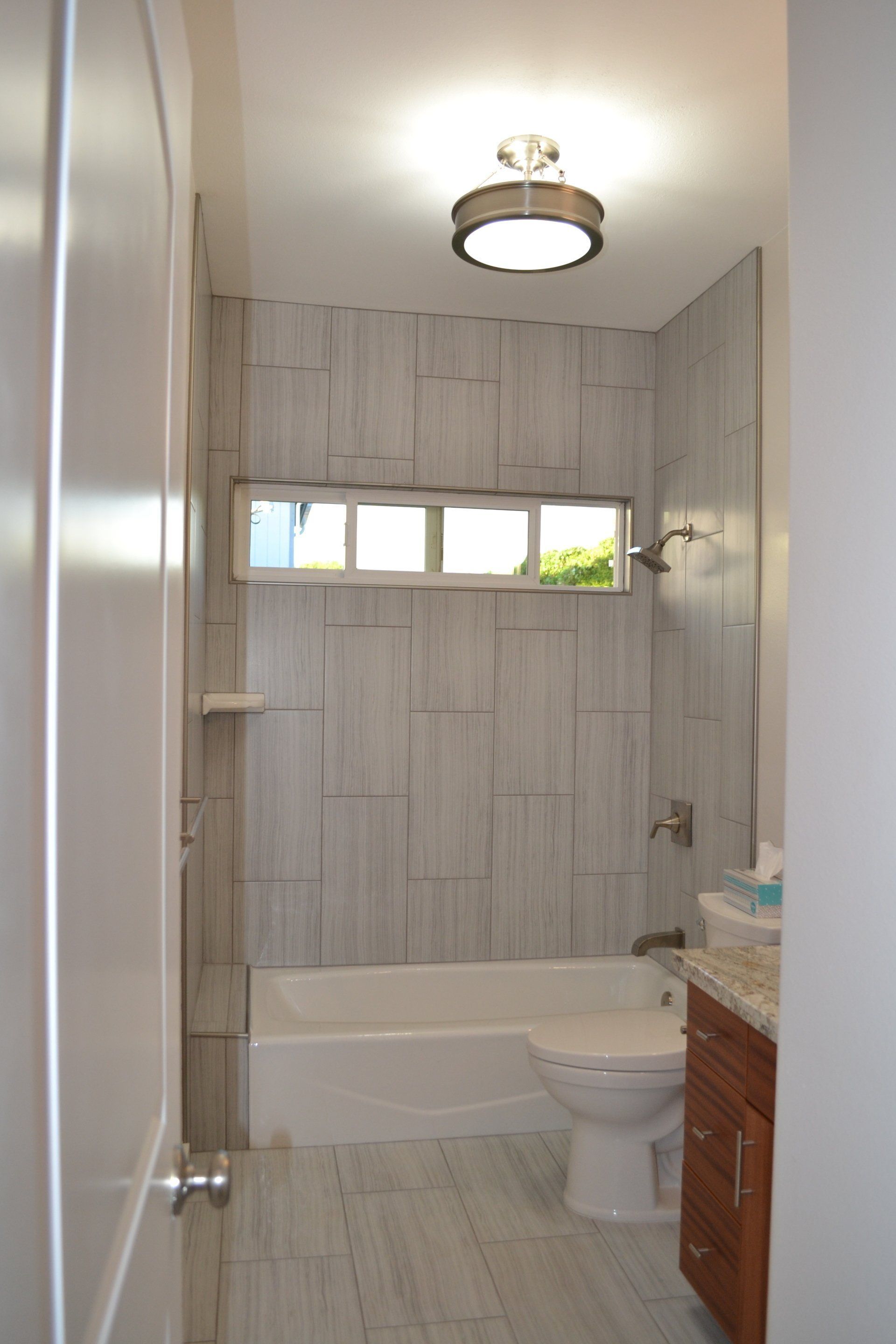 A bathroom with a toilet , tub , shower and window.