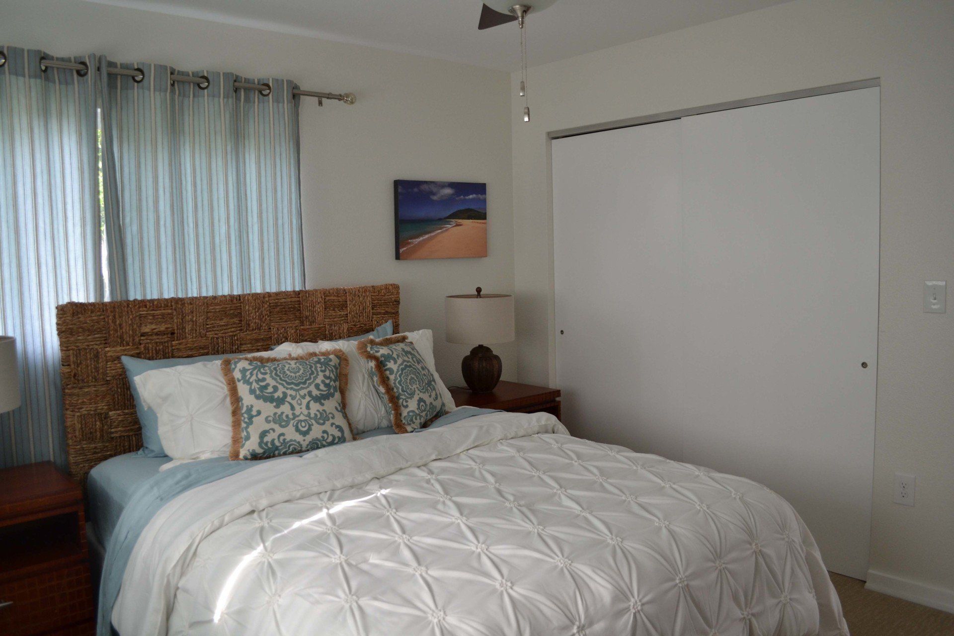 A bedroom with a bed , nightstand , lamp and window.