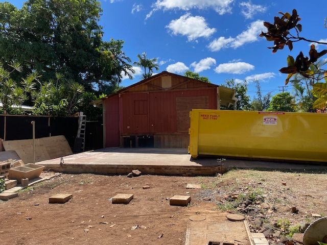 A yellow dumpster is sitting in front of a red barn.