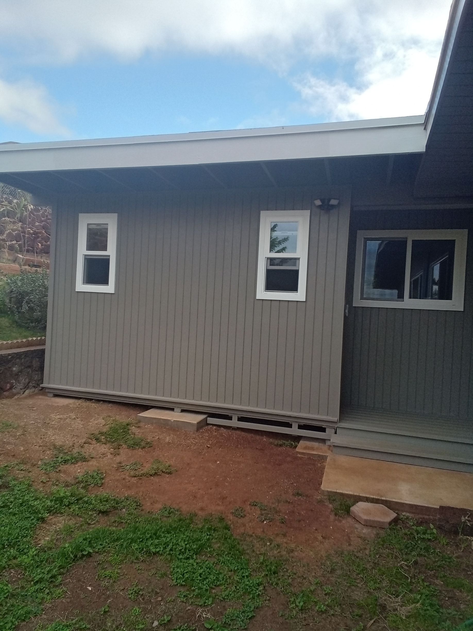 A small house with two windows is sitting in the middle of a grassy field.