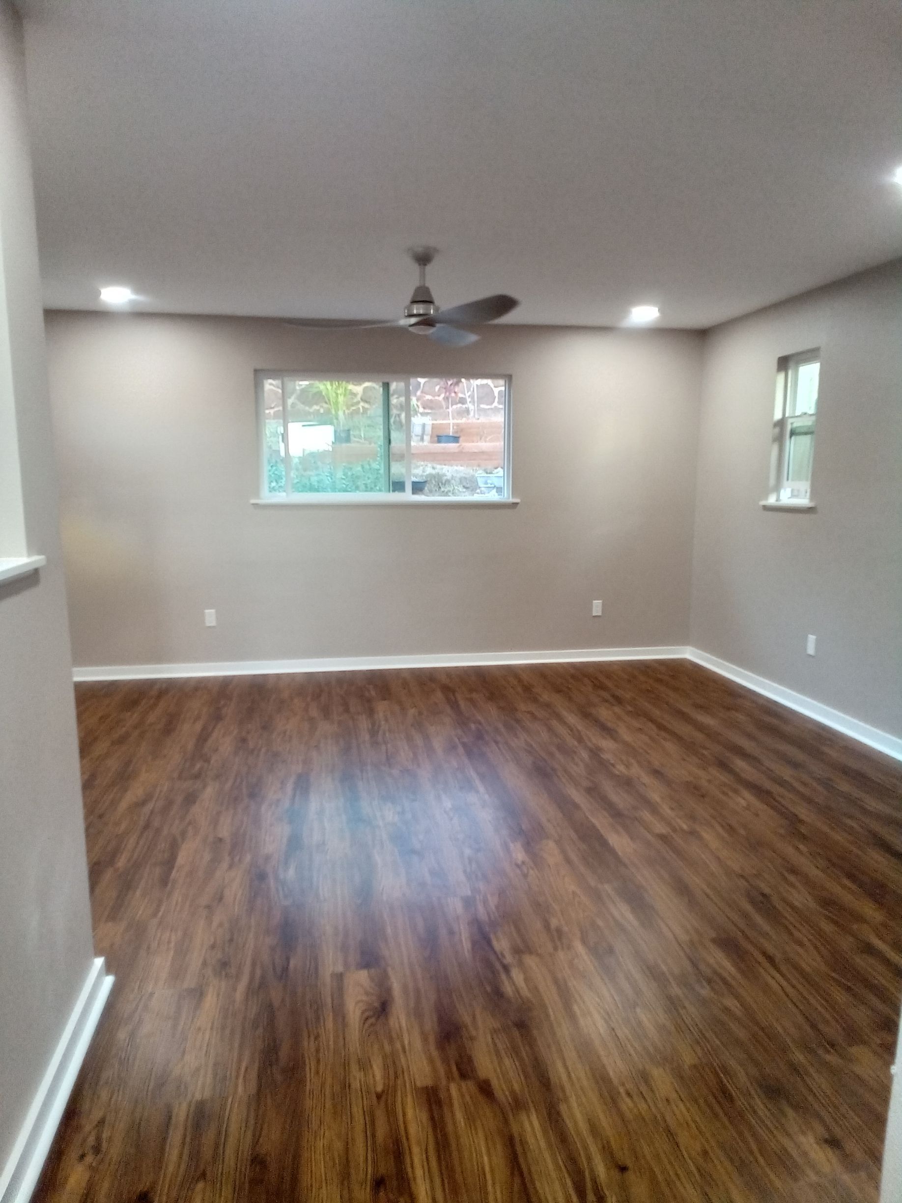 An empty living room with hardwood floors and a ceiling fan.