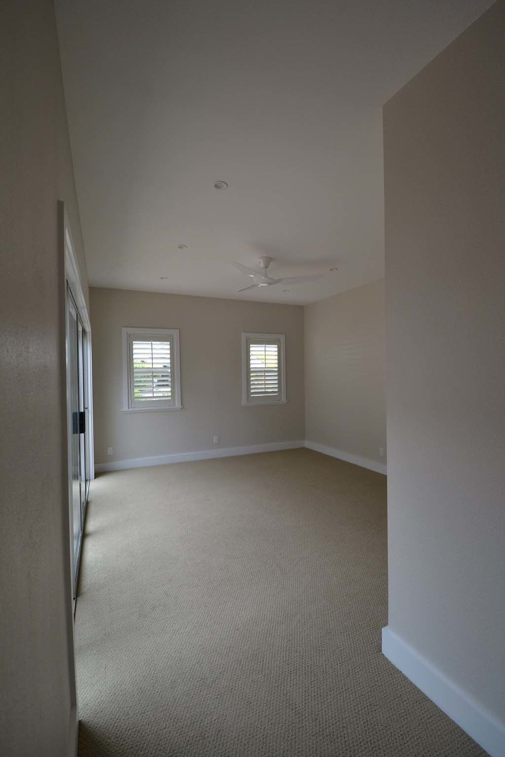 An empty room with a ceiling fan and two windows.