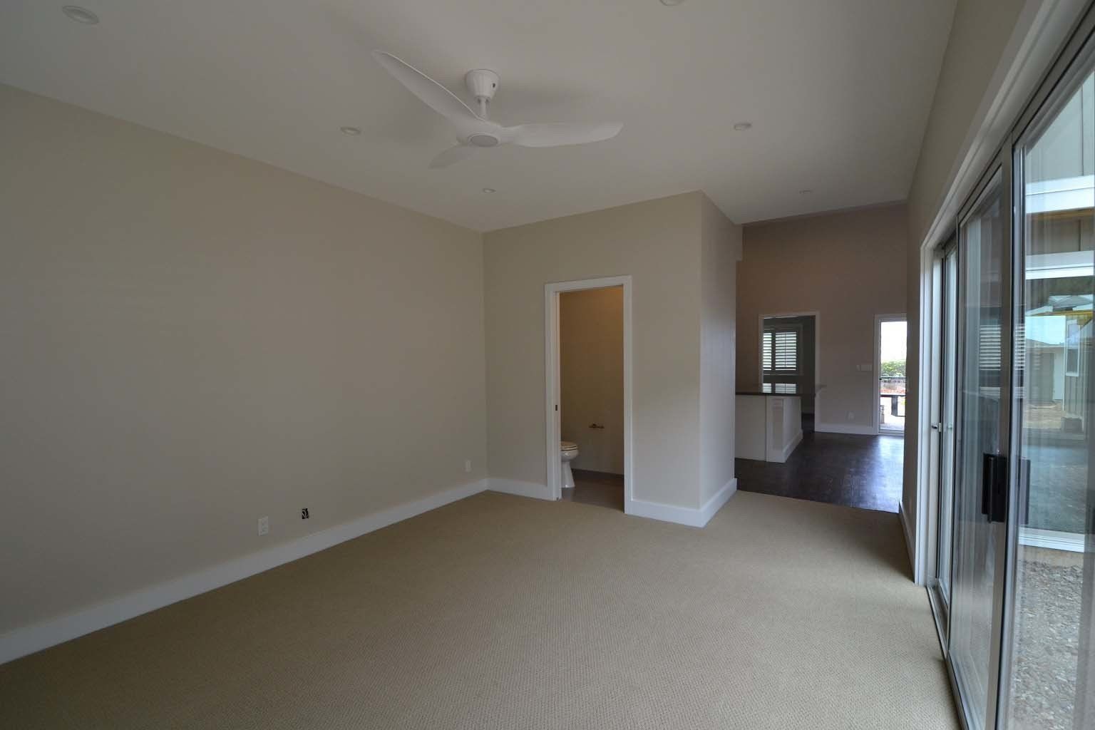 A large empty room with a ceiling fan and sliding glass doors.