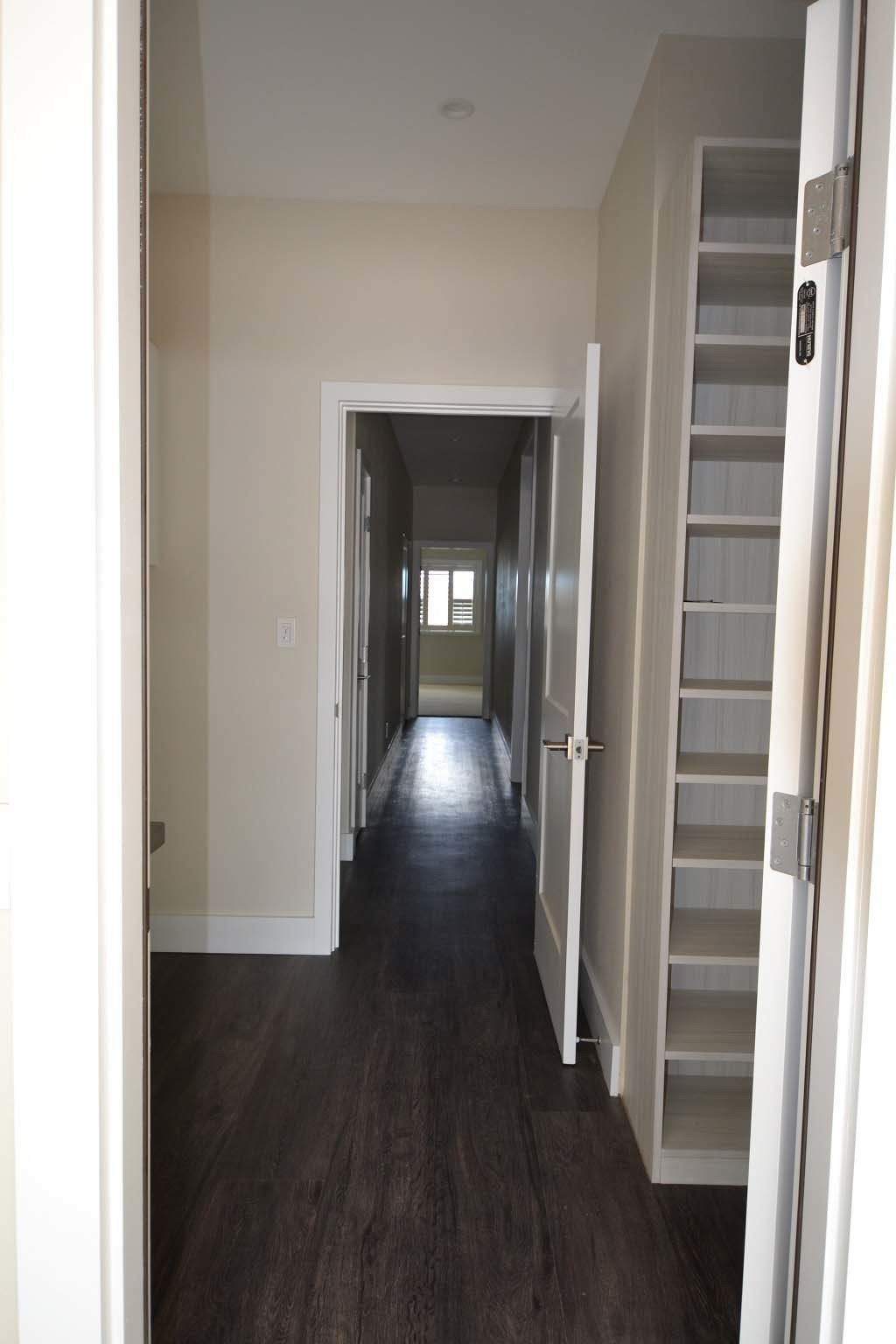 A long hallway with a shelf in the corner and a door open.
