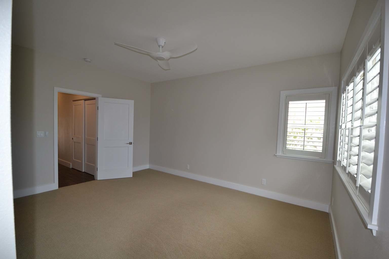 An empty bedroom with a ceiling fan and shutters on the windows.