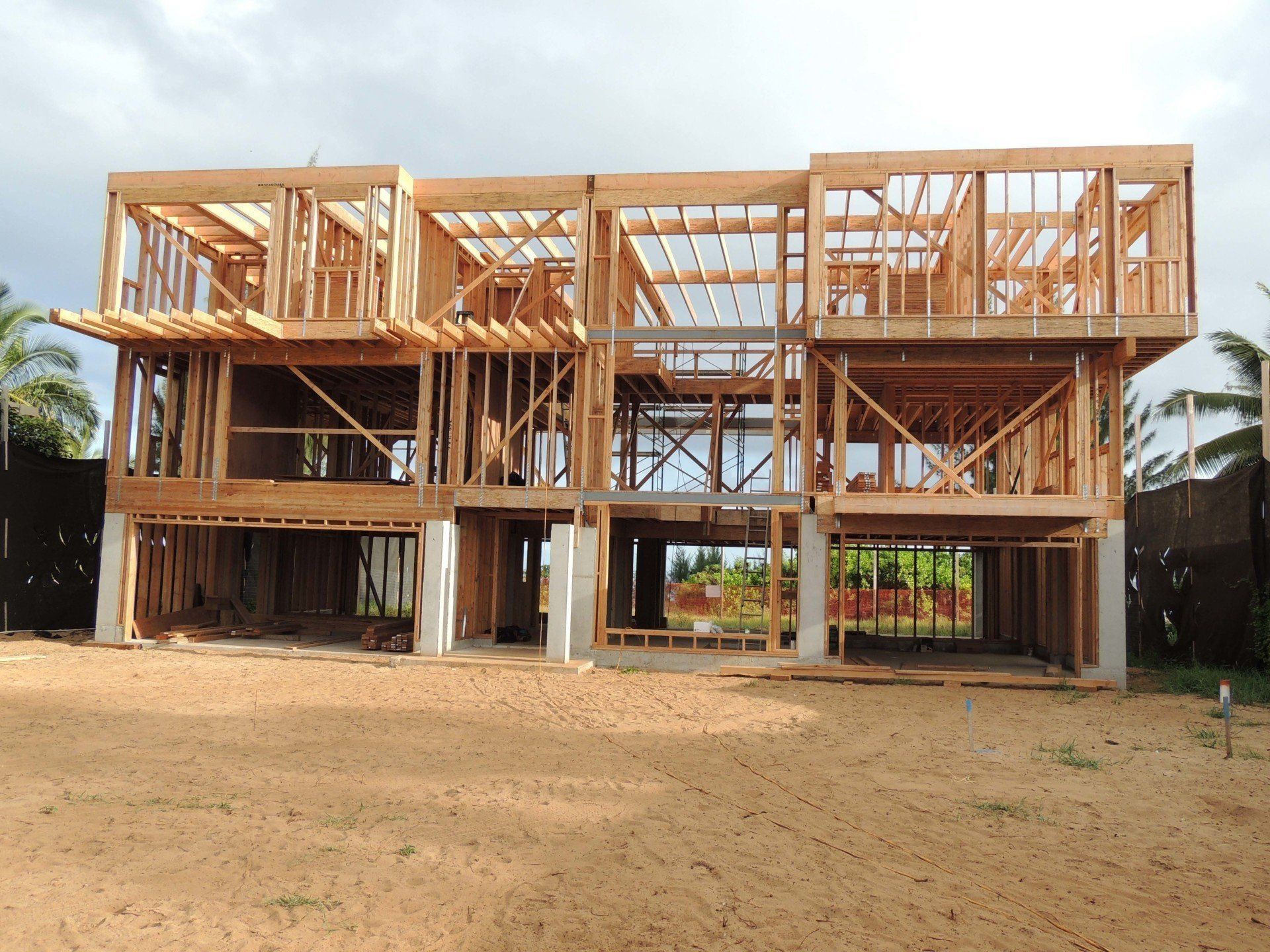 A large wooden house is being built in a dirt field