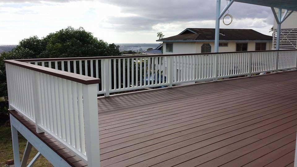 A wooden deck with a white railing and a house in the background