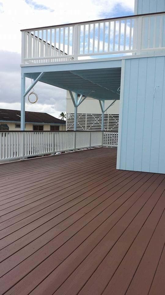 A wooden deck with a white railing and a blue building in the background.