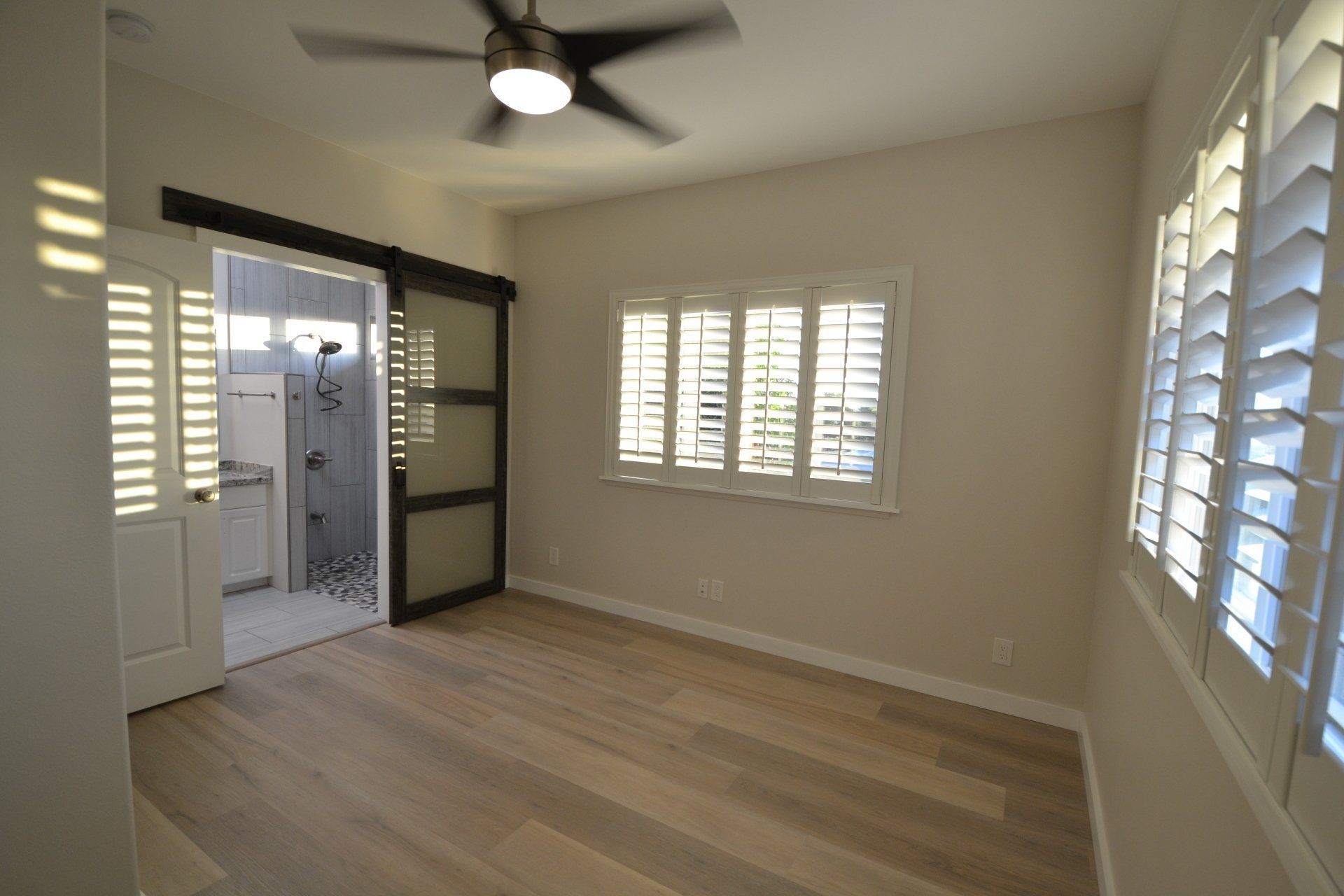 An empty room with a ceiling fan and shutters on the windows.