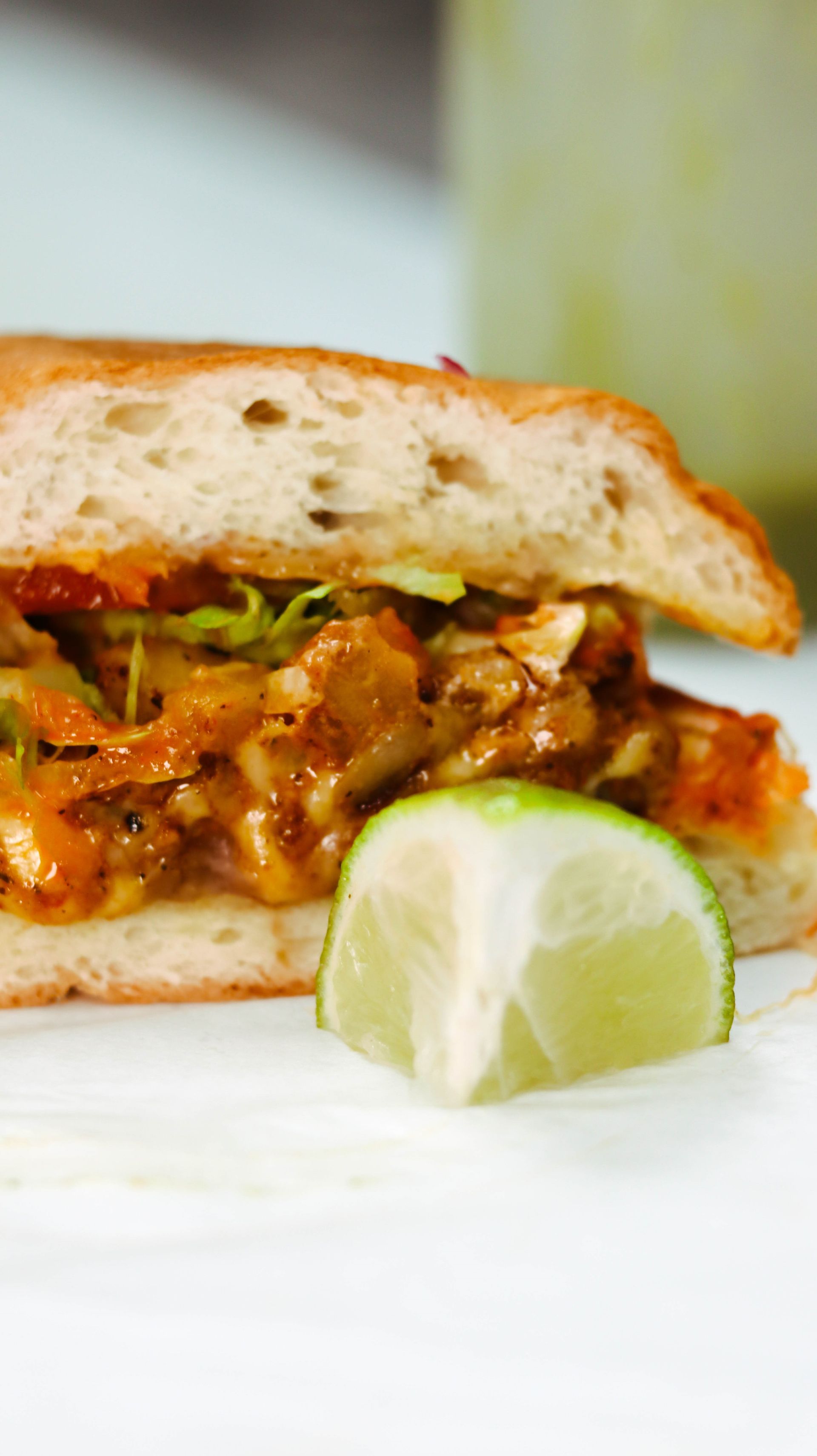 A close up of a sandwich with a slice of lime on a plate.