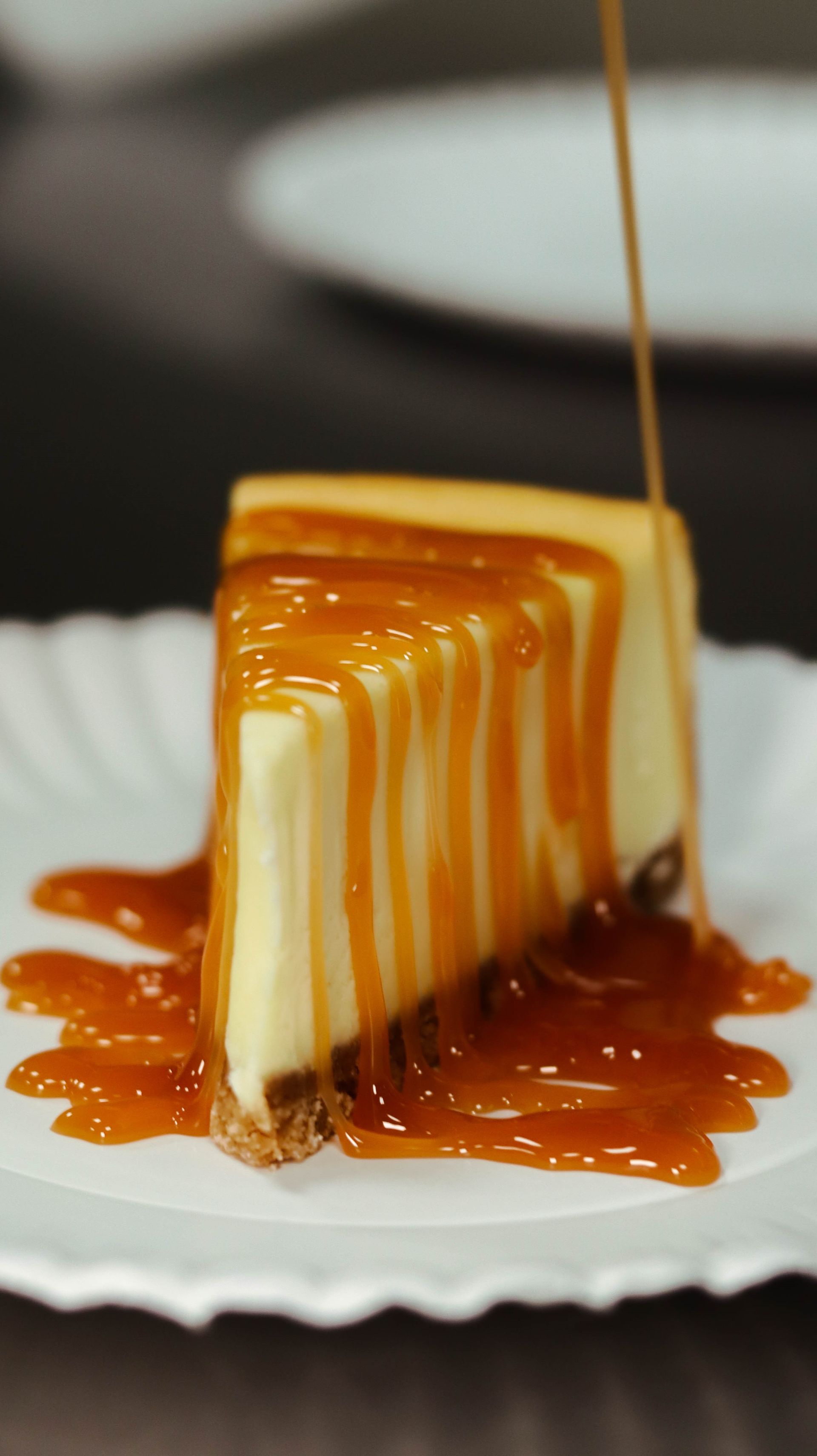 A slice of cheesecake with caramel sauce on a paper plate.