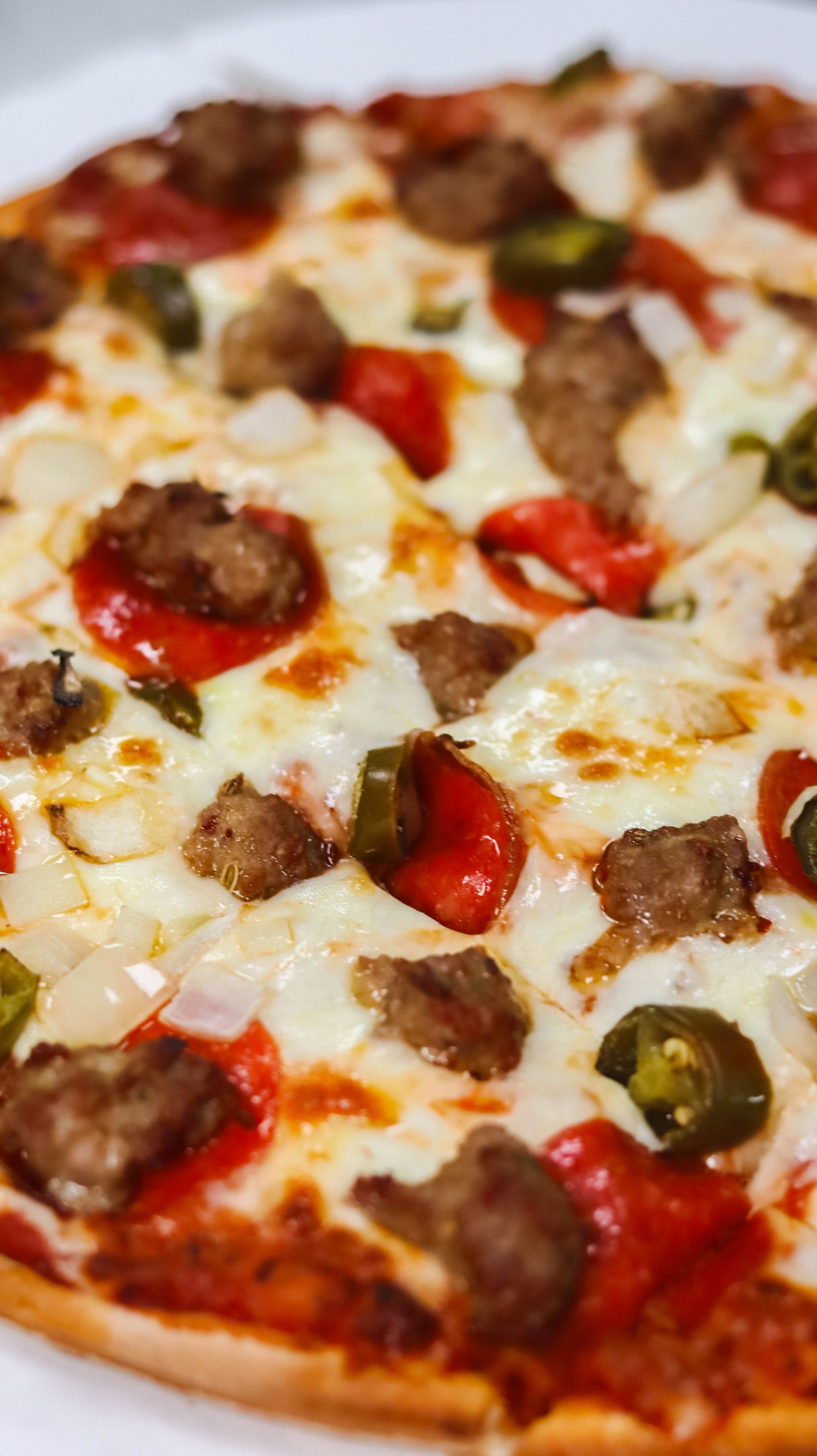 A pizza with sausage , peppers , onions and cheese on a white plate.
