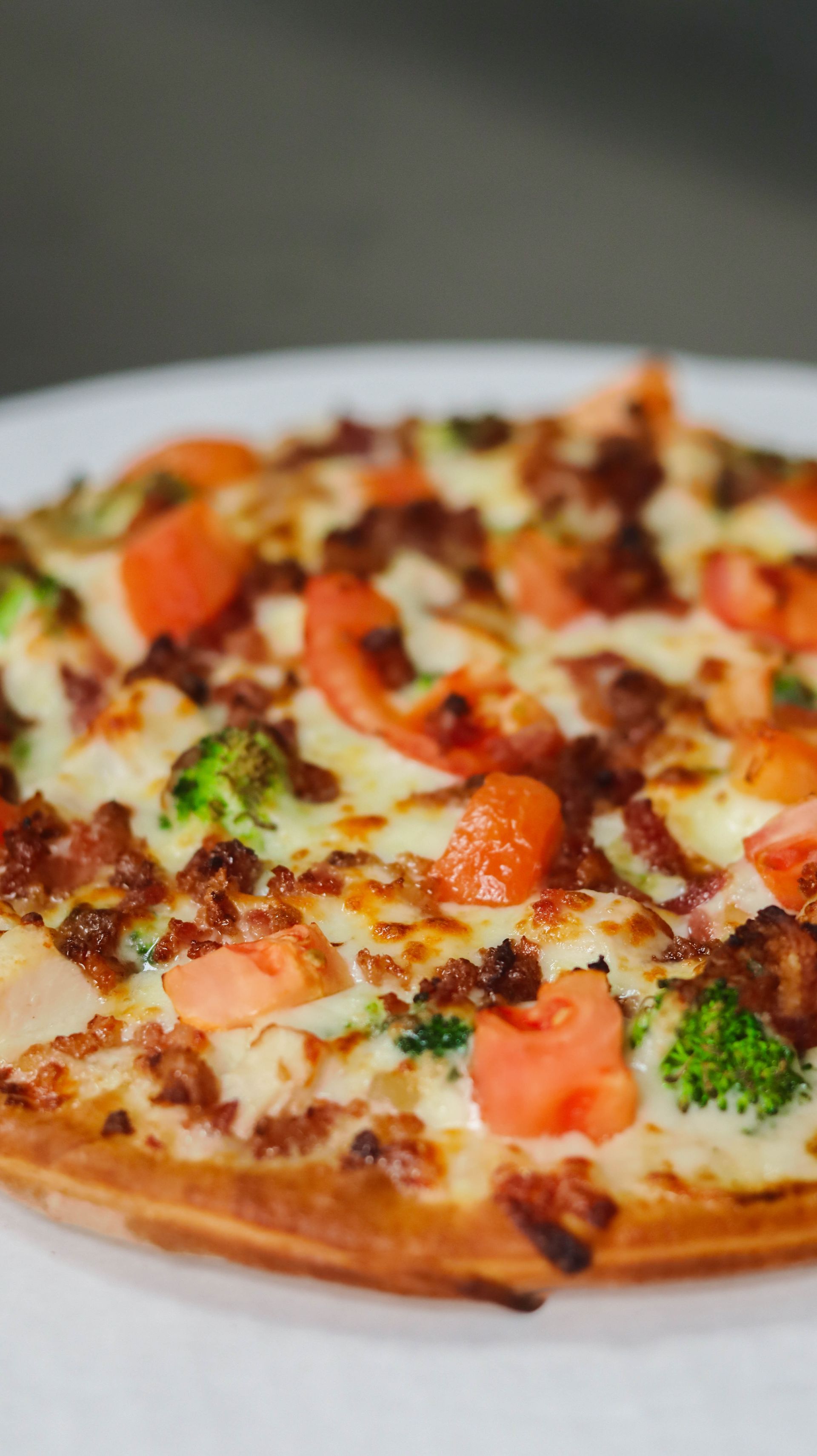 A pizza with broccoli , tomatoes , bacon and cheese on a white plate.