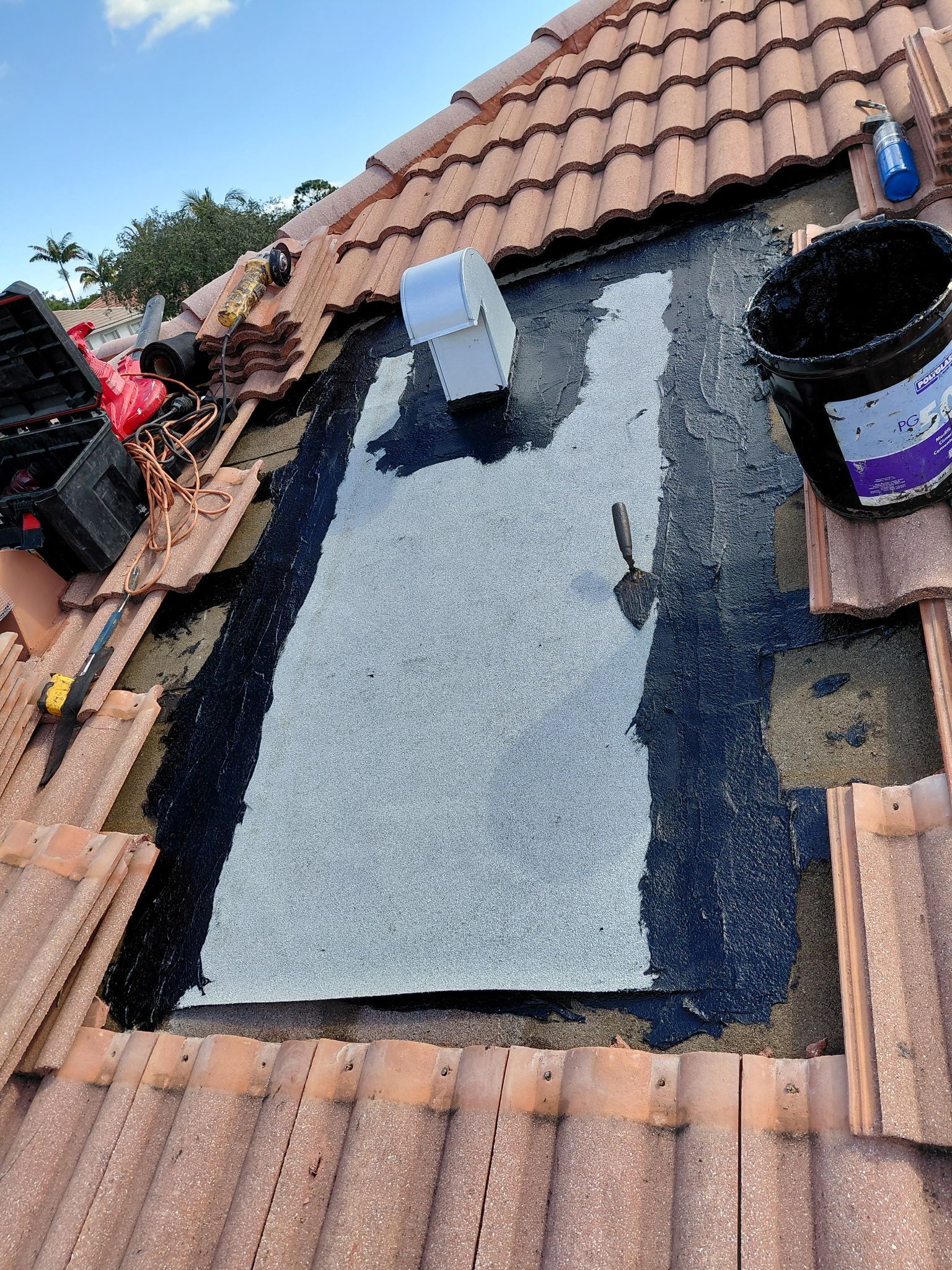 Roofer applying black waterproof coating on a flat roof between terracotta tiles