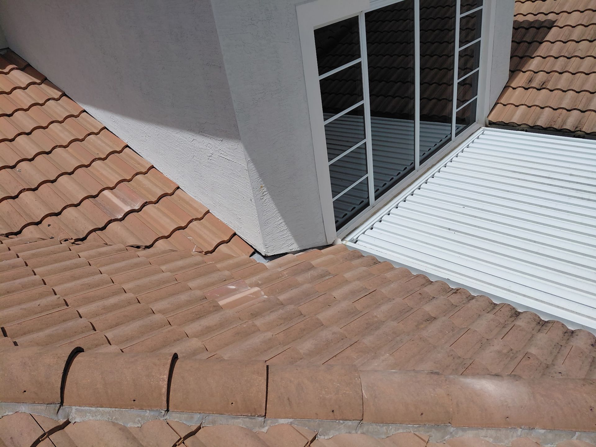 Rooftop with terracotta and white metal sections beside a windowed dormer.