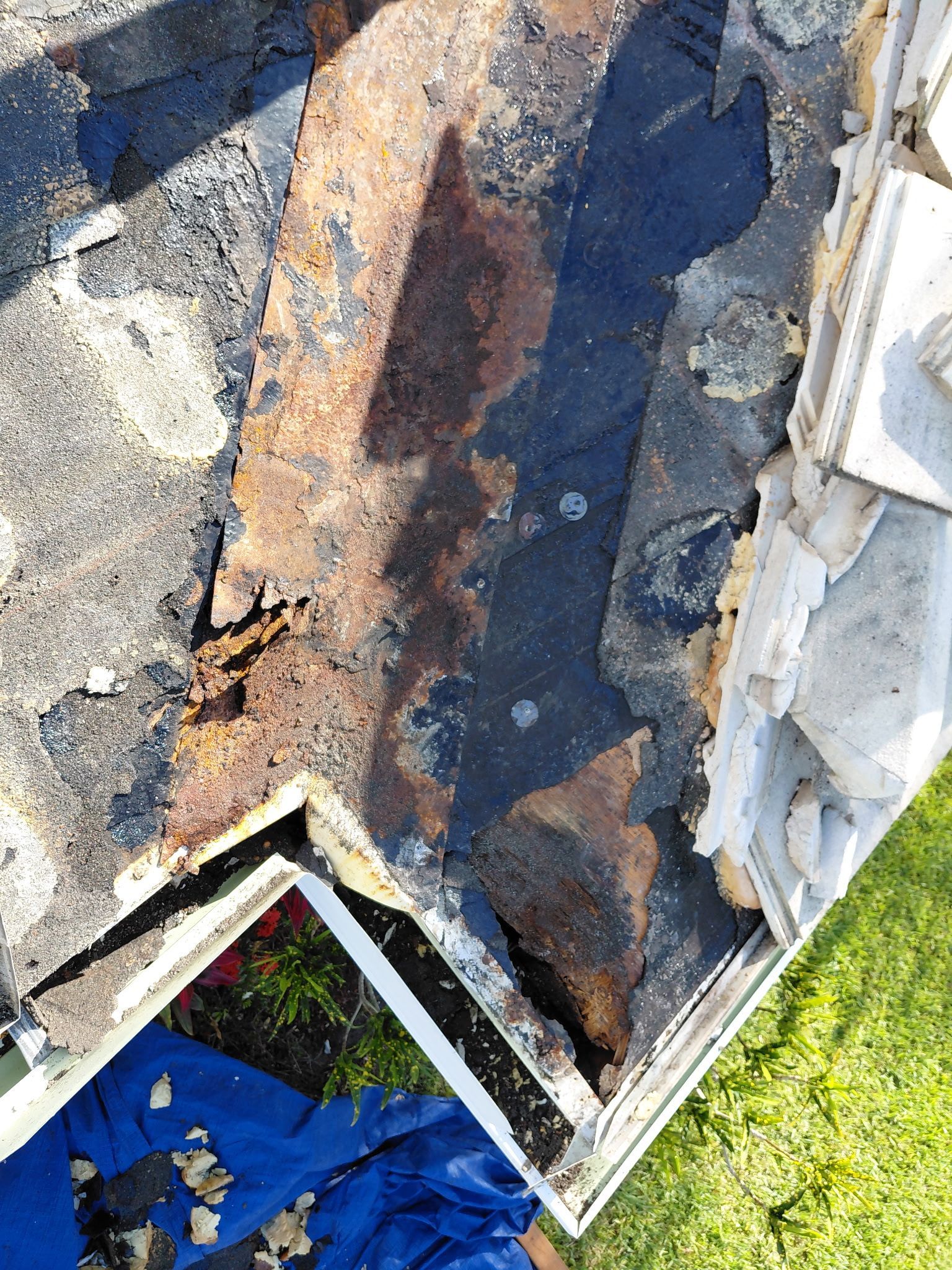 Damaged roof shingles with peeling, weathered surfaces and debris near a roof edge