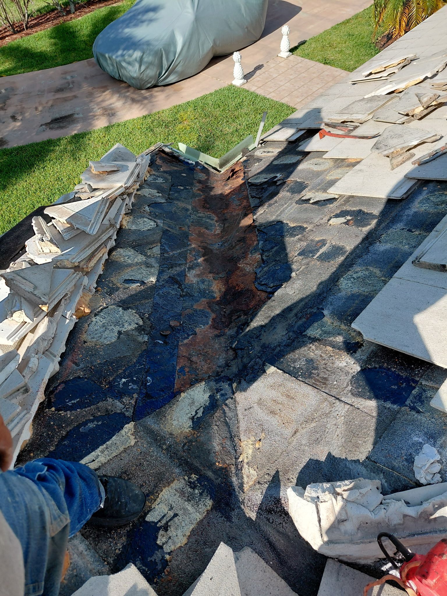 Damaged roof with torn black underlayment and exposed shingles beside a lawn and driveway