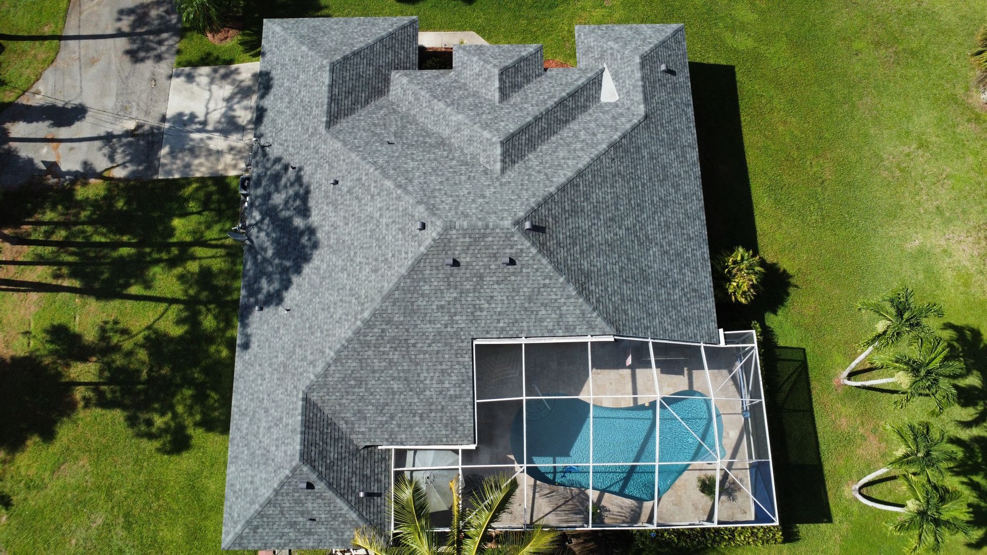 Aerial view of a gray shingled house with a screened-in blue pool patio and surrounding green lawn.